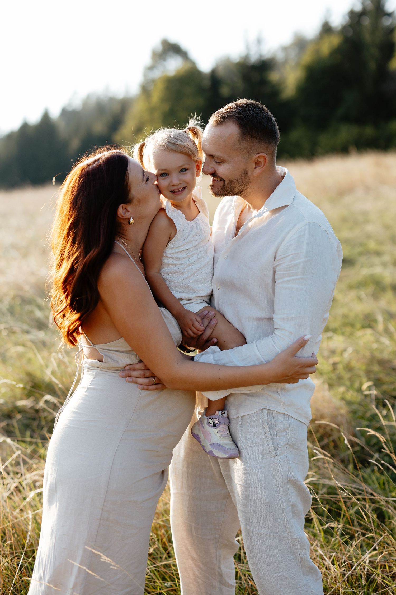 A family shares tender moments together in a sunlit field wearing white and beige outfits.