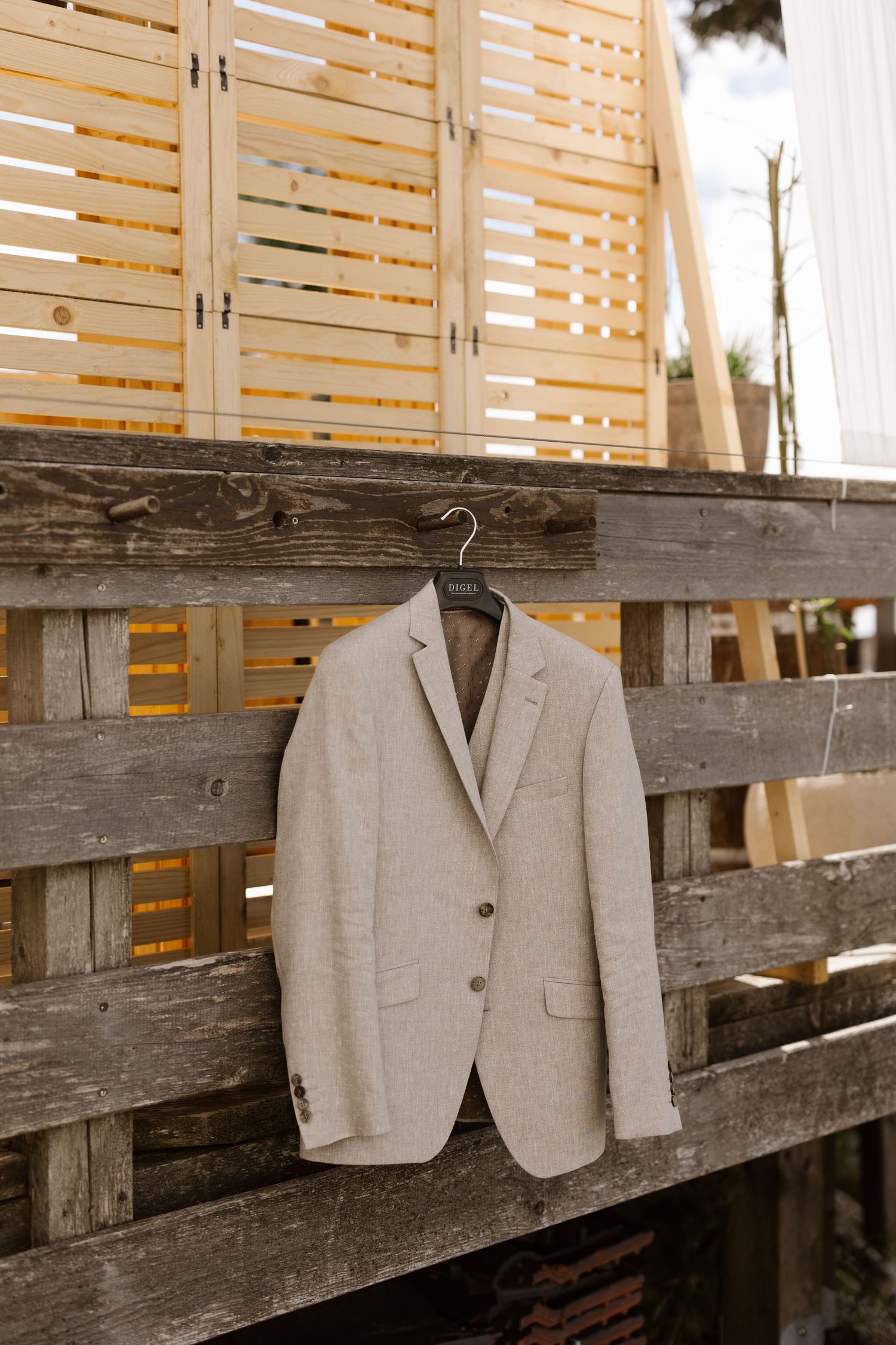 Light colored formal suit jacket hanging on wooden slats in natural lighting.