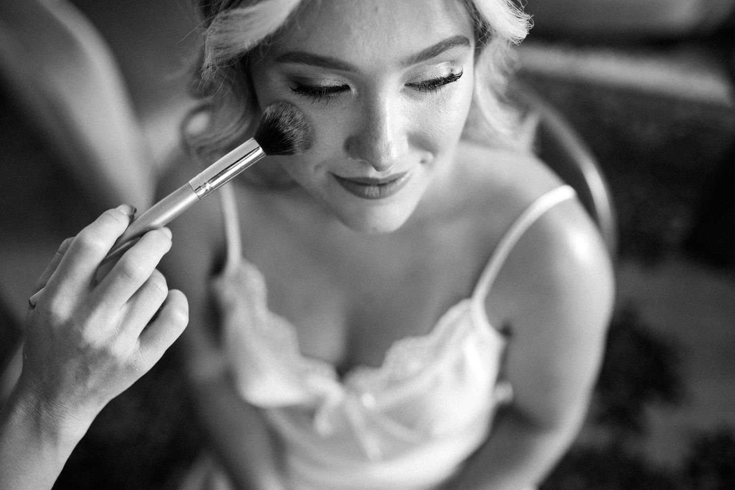 Black and white photo showing makeup application with brush in soft natural lighting.