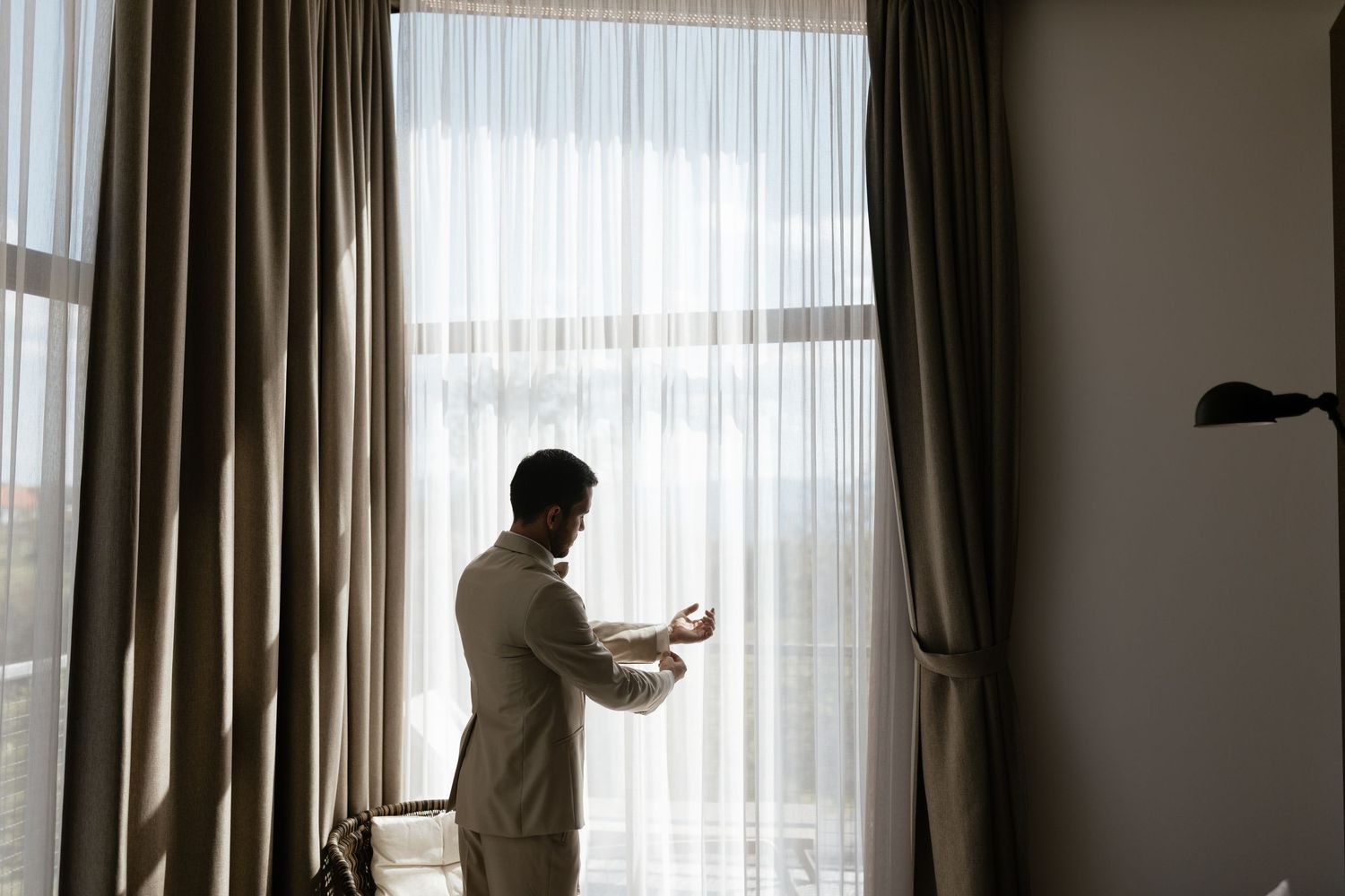 Silhouette of person opening curtains by large window in morning light, creating a peaceful morning atmosphere.