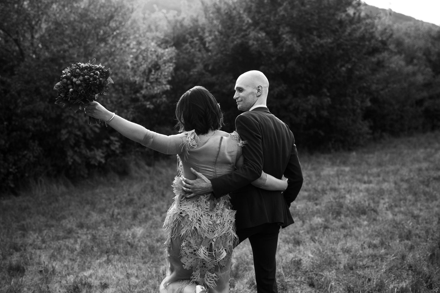 A couple dances joyfully together in a field during sunset with mountains in the background.