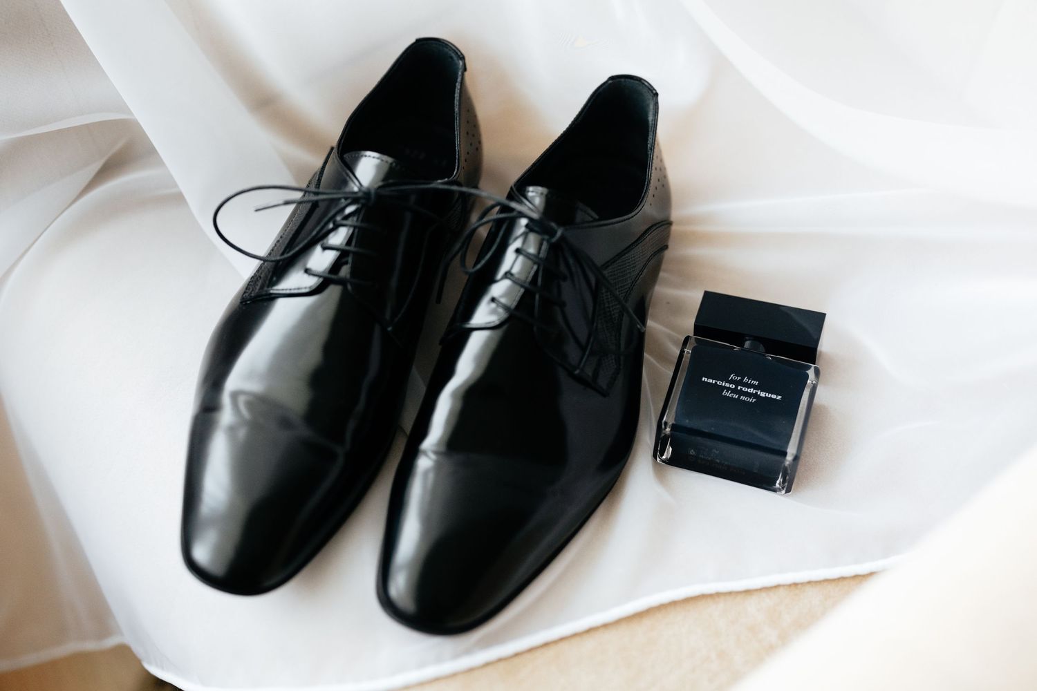 A pair of black leather dress shoes with laces arranged on white fabric with small product boxes in the background.