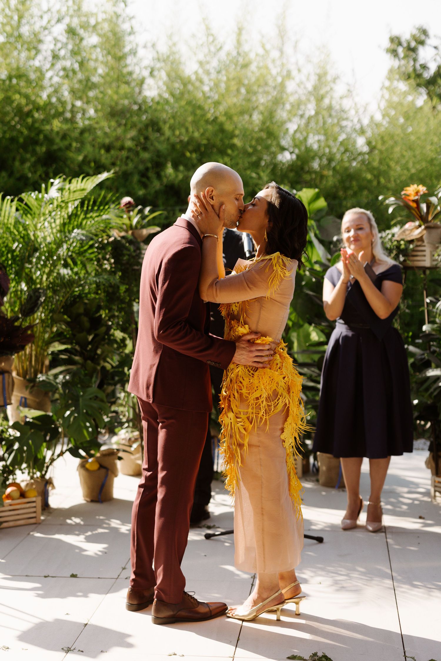 A couple shares a romantic moment in a garden setting while someone watches with joy.
