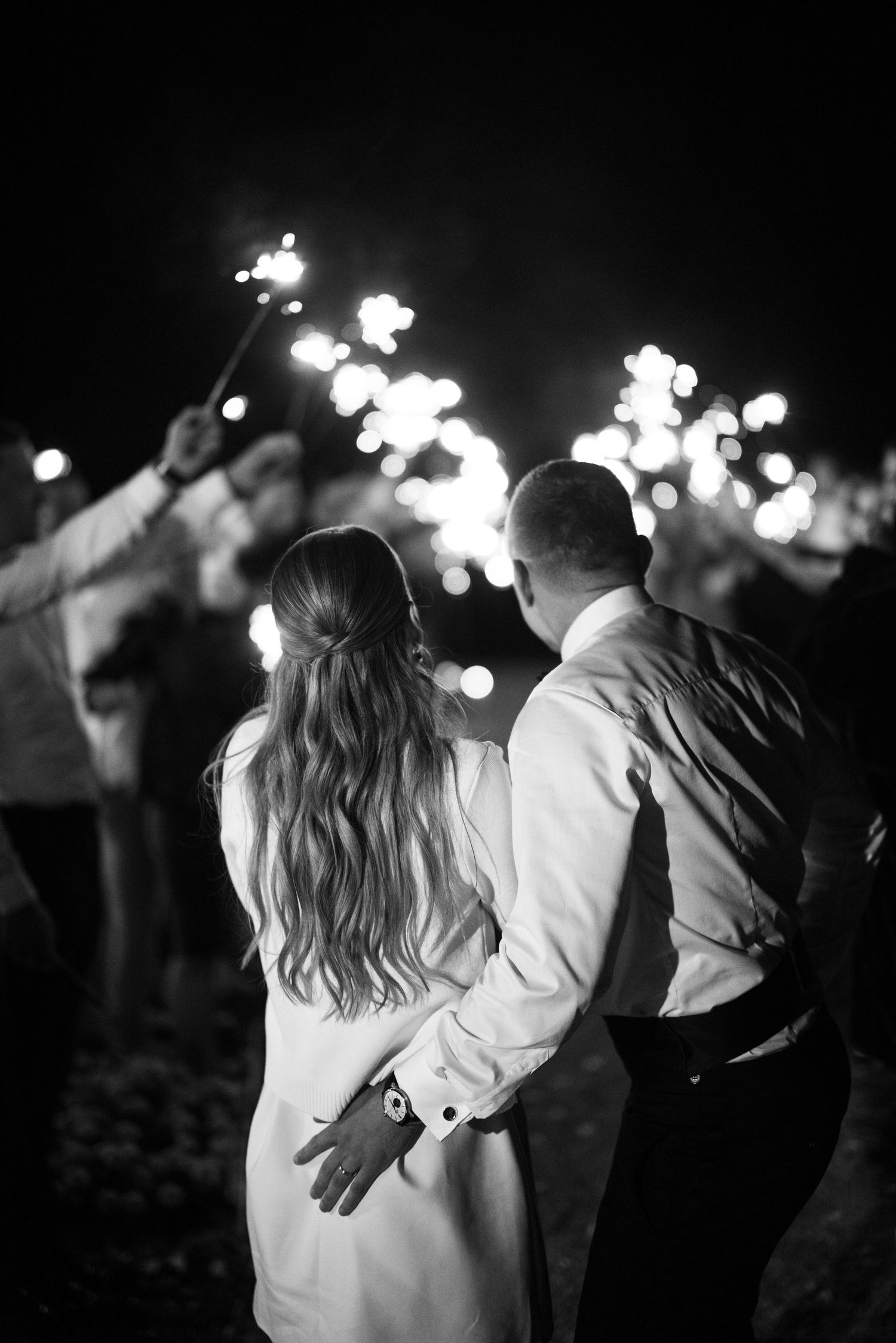 Black and white nighttime wedding celebration with sparklers creating bokeh effects.