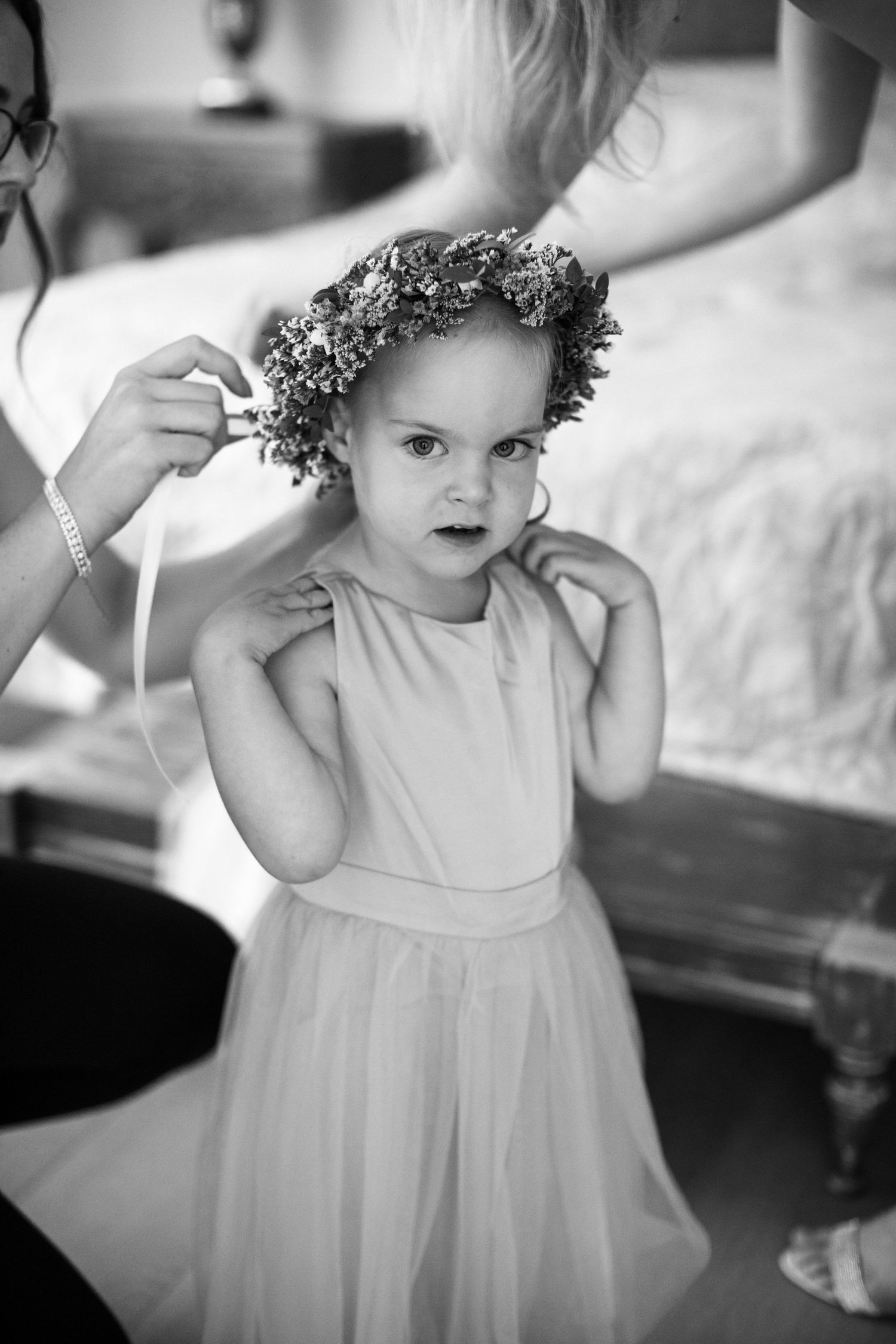 Black and white portrait of a small child wearing a white dress and floral crown at a formal event.