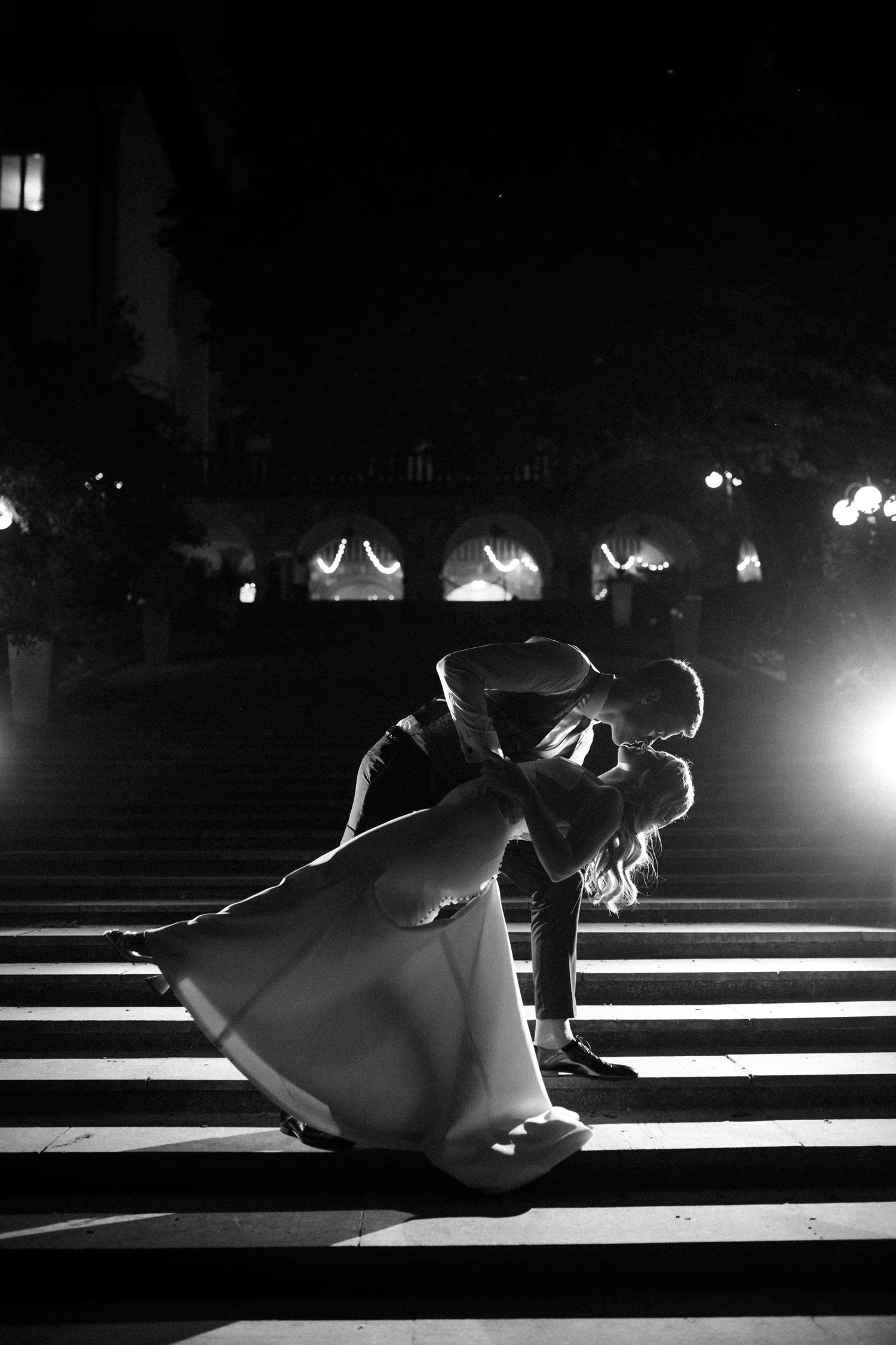A dramatic black and white dance dip pose on illuminated steps at night.