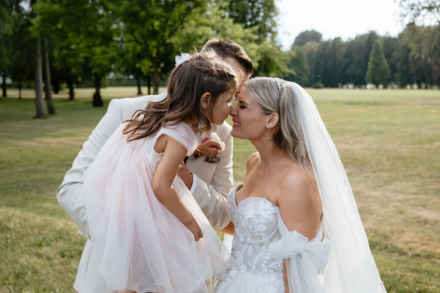 Bride and flower girl share a tender moment outdoors in a sunlit garden setting.
