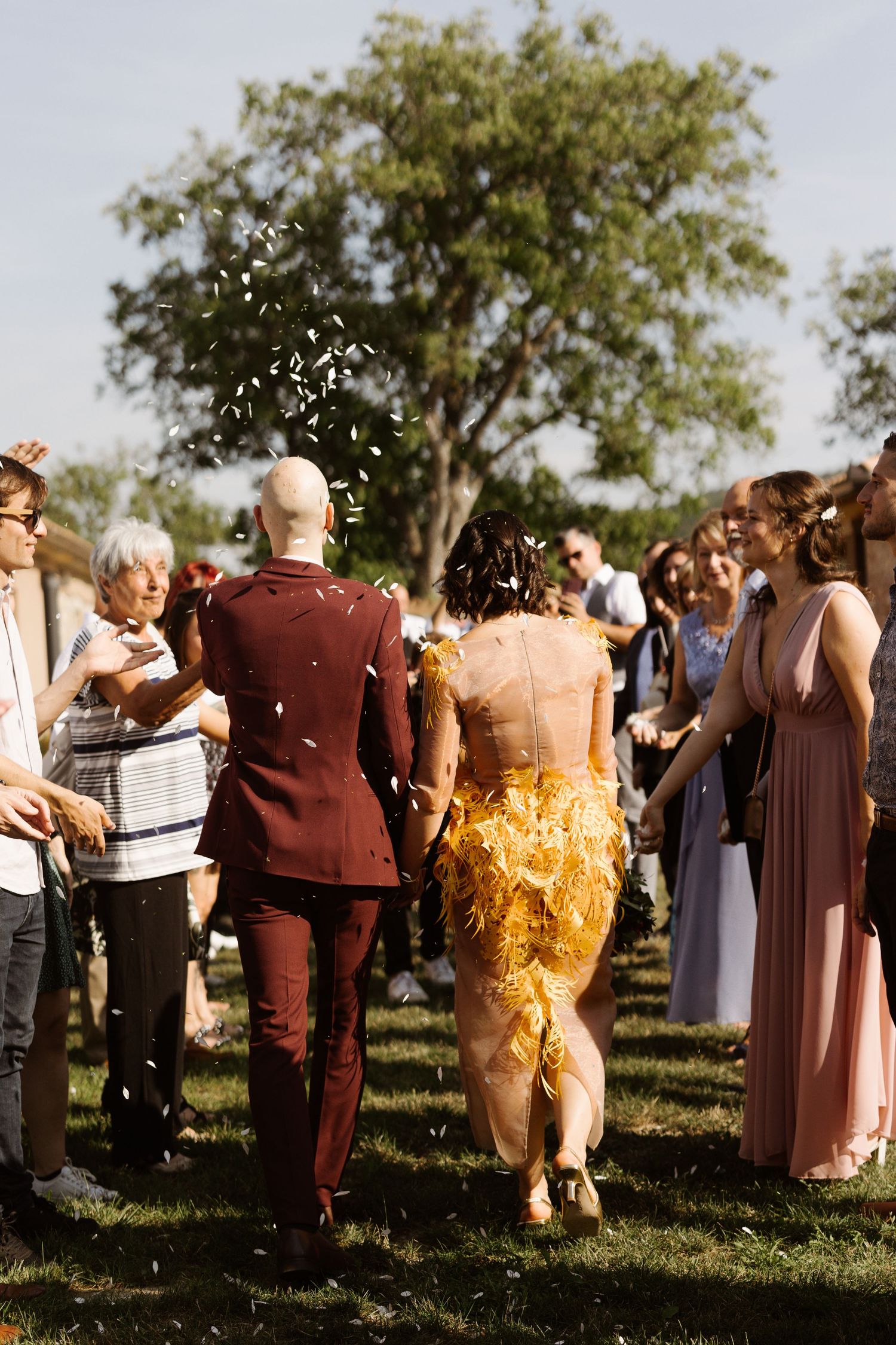 Wedding guests gathered outdoors in burgundy and neutral attire during a sunny celebration.