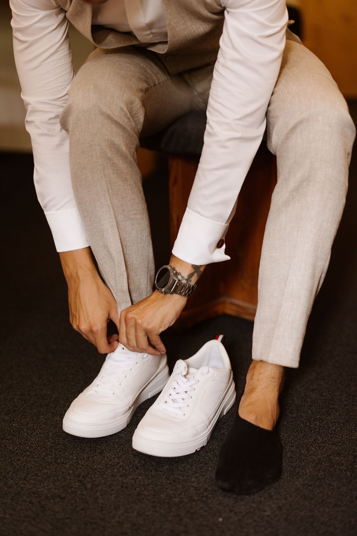Close-up of hands putting on white sneakers and dress shoes with light gray formal attire.