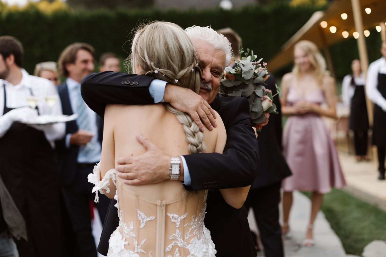 Wedding couple shares a romantic first dance outdoors at sunset while guests watch from the background.