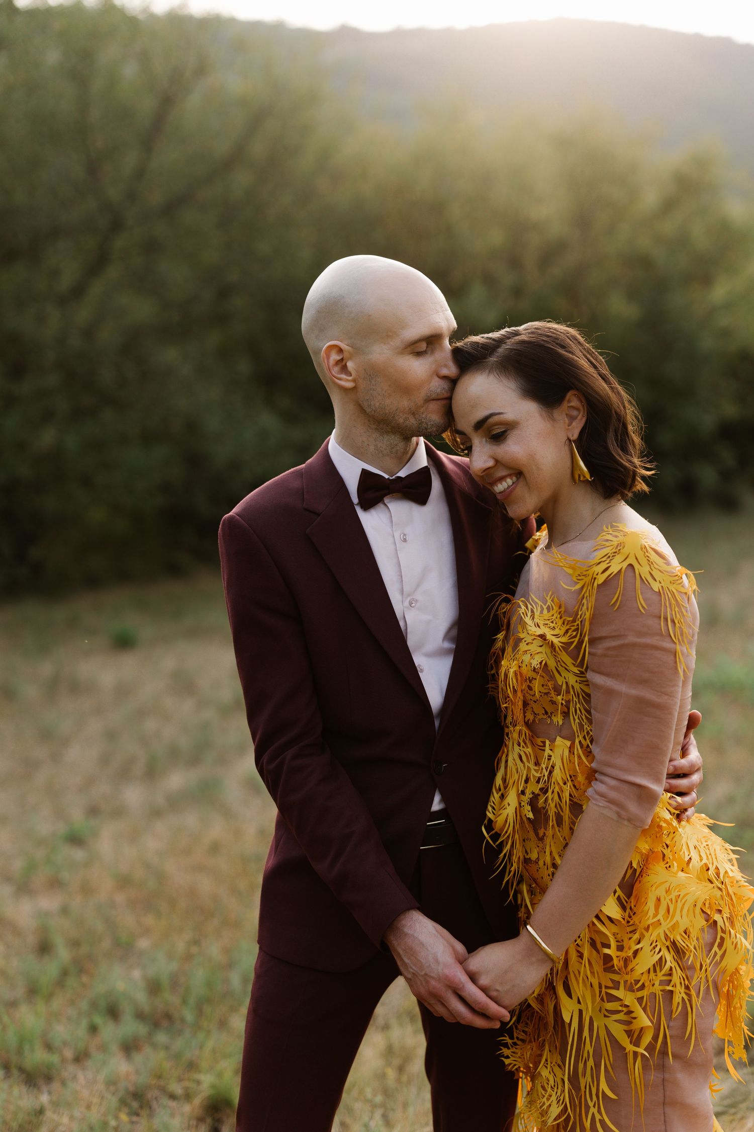 Romantic couple in formal attire embracing at sunset in a golden field.
