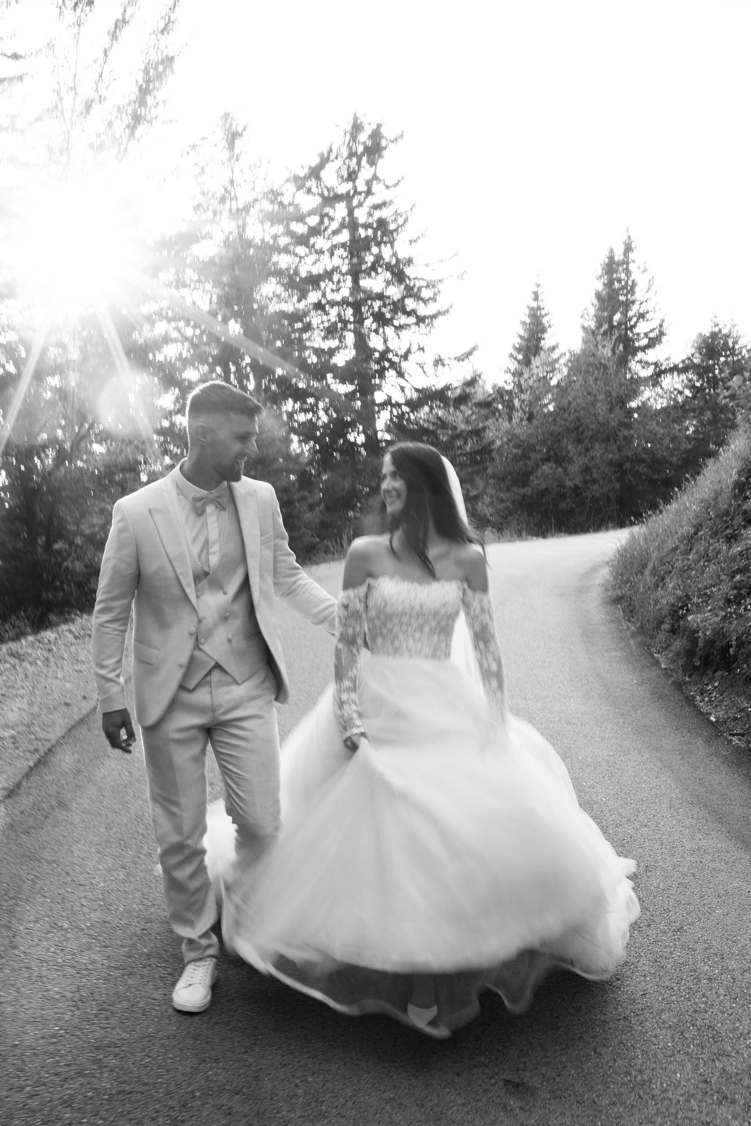 Black and white photo of a couple walking together on a winding mountain road in wedding attire.