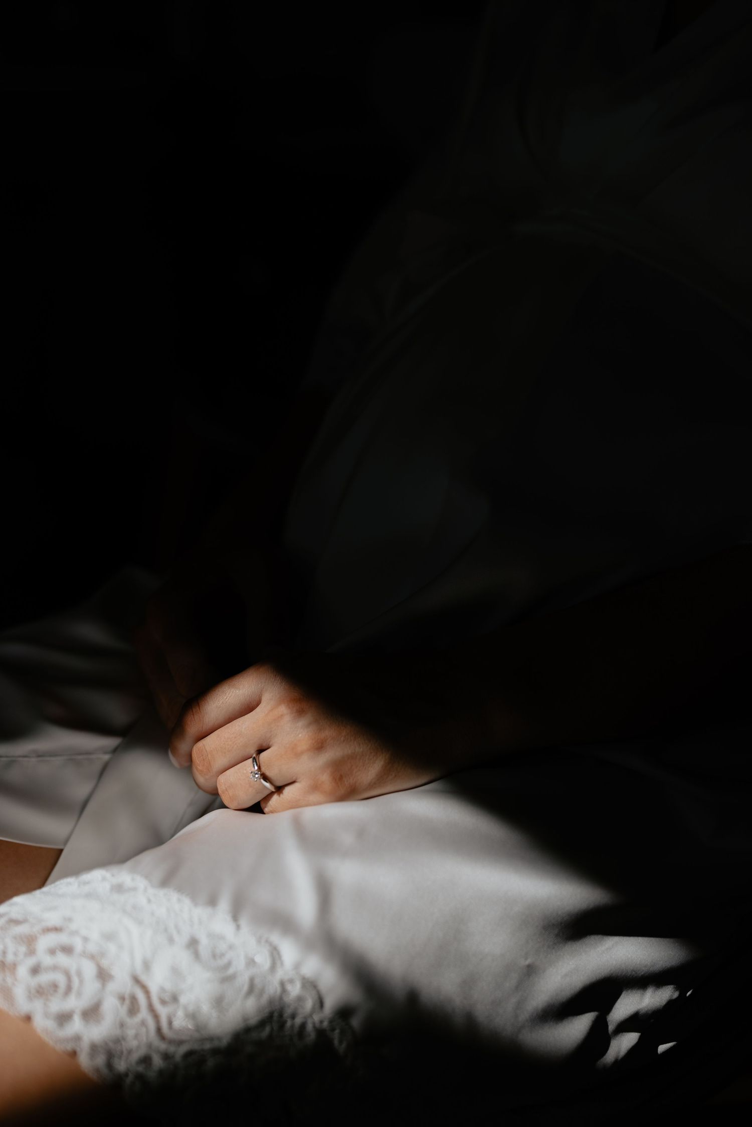 A close-up view of white lace gloves worn on hands against a dark background, highlighting delicate floral patterns.