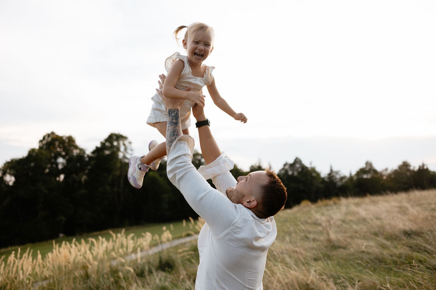 A joyful moment as a parent lifts their child high into the air in an outdoor field.