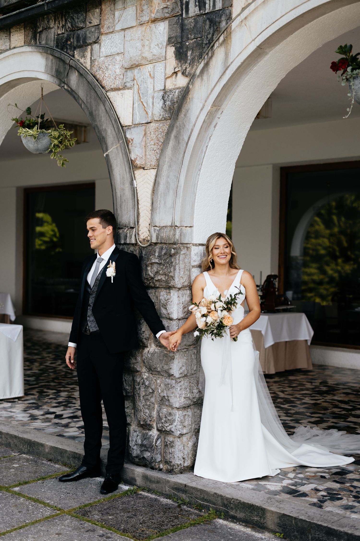 Newlyweds stand elegantly under stone archways with white columns at their wedding venue.