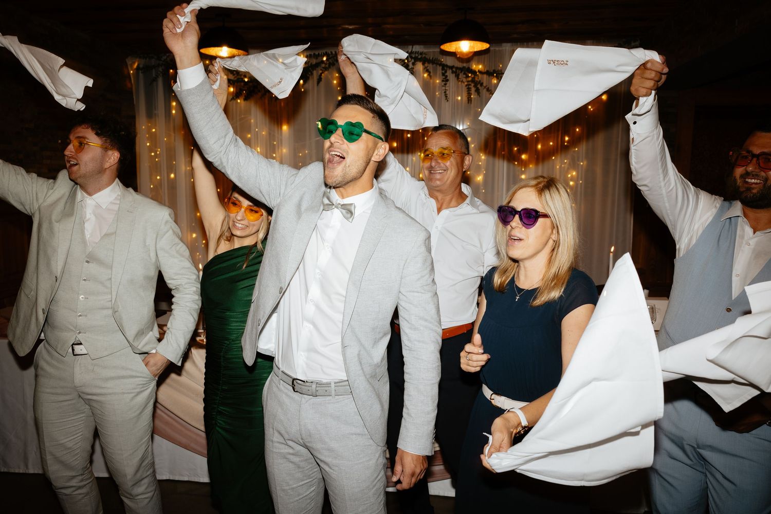 Wedding reception celebration with guests waving napkins in the air during a festive party moment.