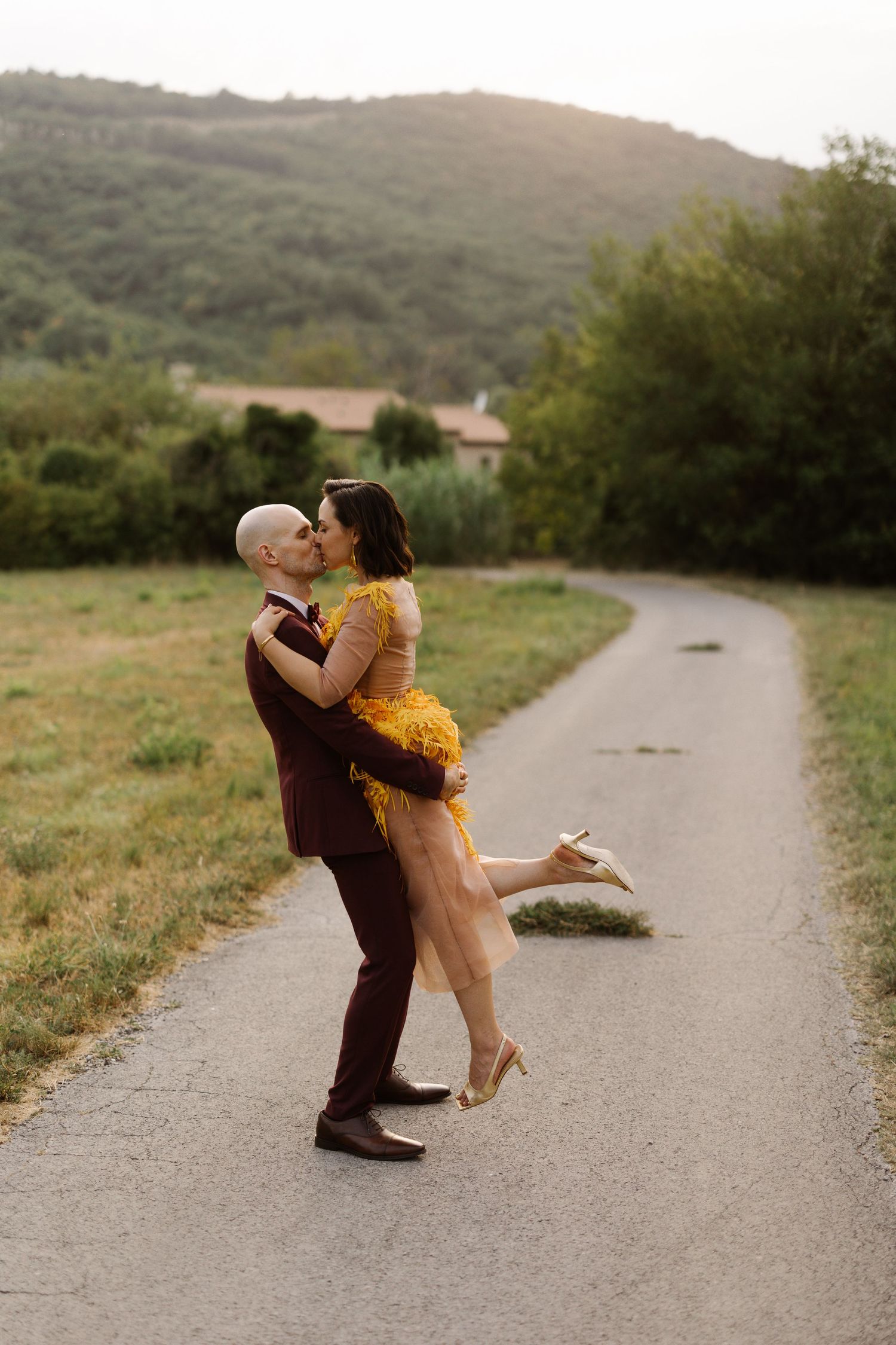 Dancing couple in formal attire sharing playful moments on a country road at sunset.