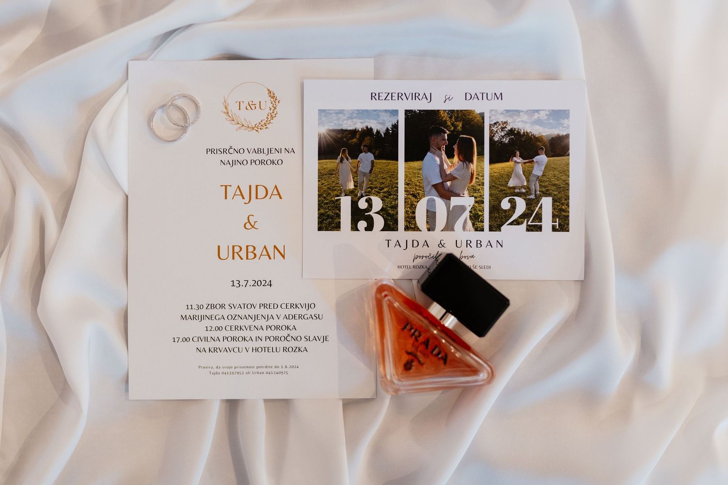 Elegant perfume bottles and wedding invitation cards arranged on white fabric in soft lighting.