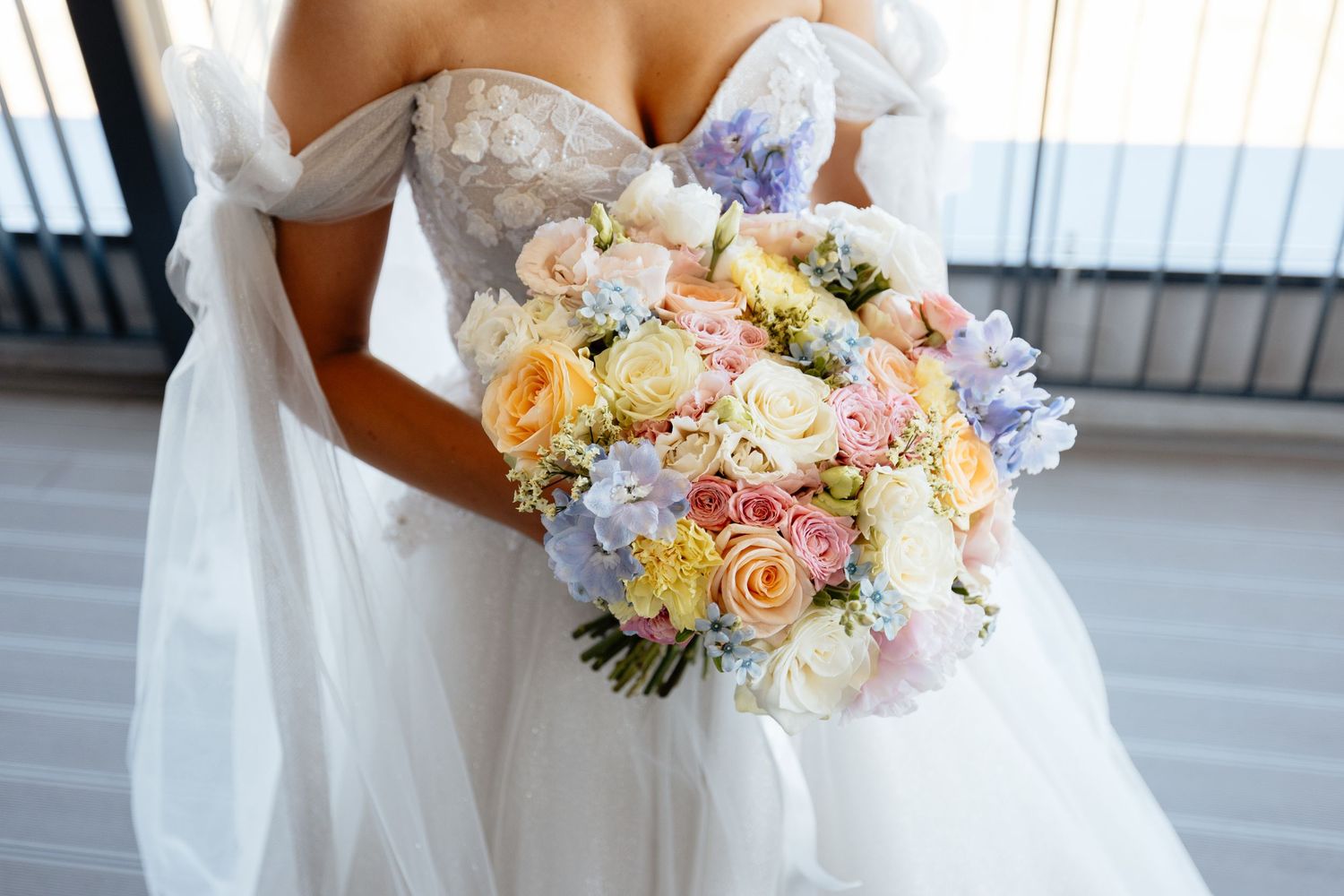 Close-up view of a pastel pink and peach bridal bouquet with roses and delicate flowers against a white dress.