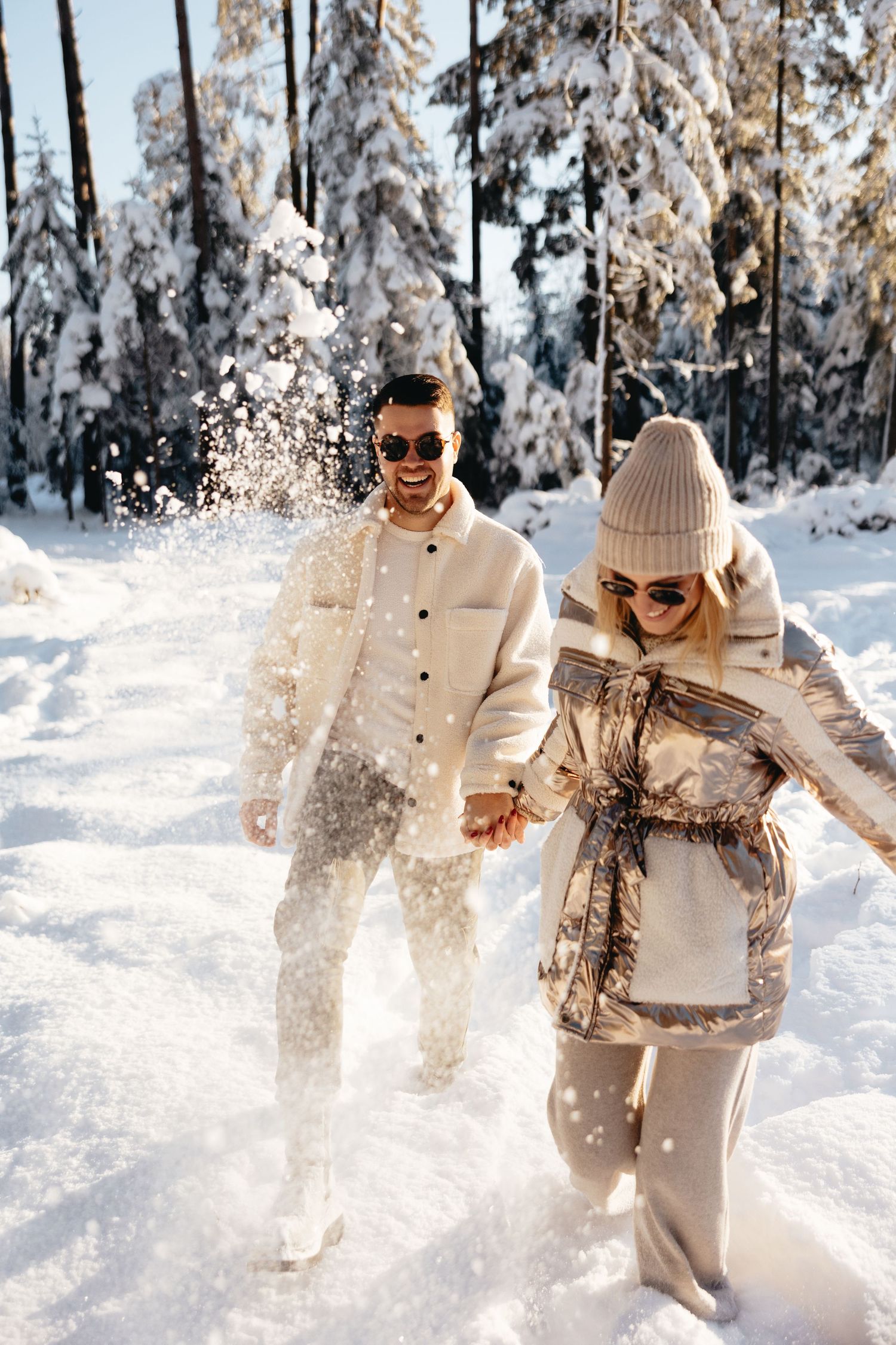 Couple in white outfits playing in the snow among frost-covered trees.