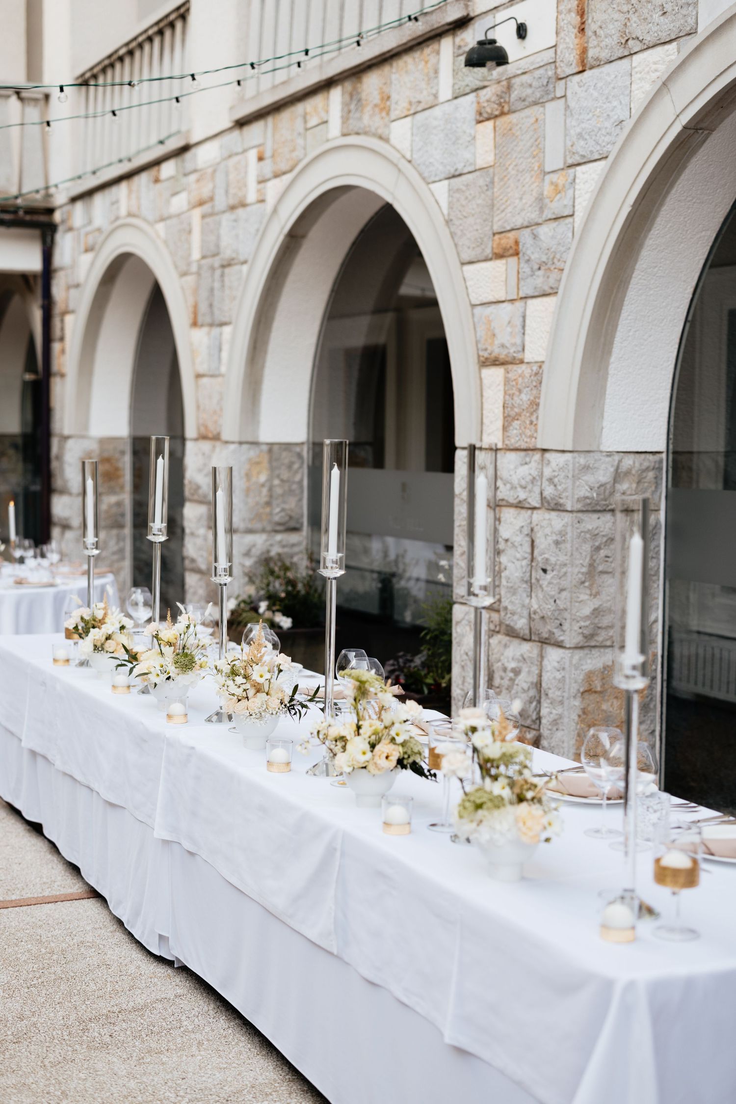 Elegant wedding reception table setup with white linens under stone archways.