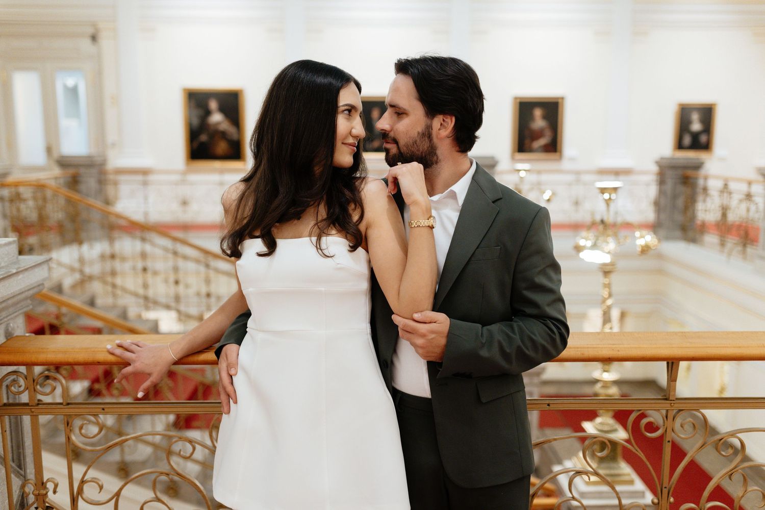 Elegant couple sharing an intimate moment in a grand white interior with ornate details.