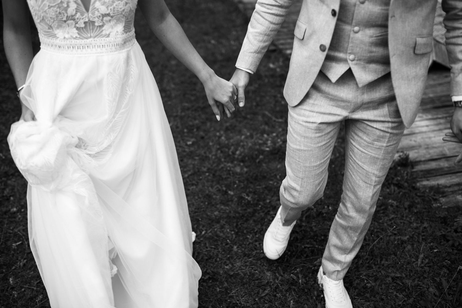 Black and white photo showing wedding couple's legs and clasped hands while walking together.