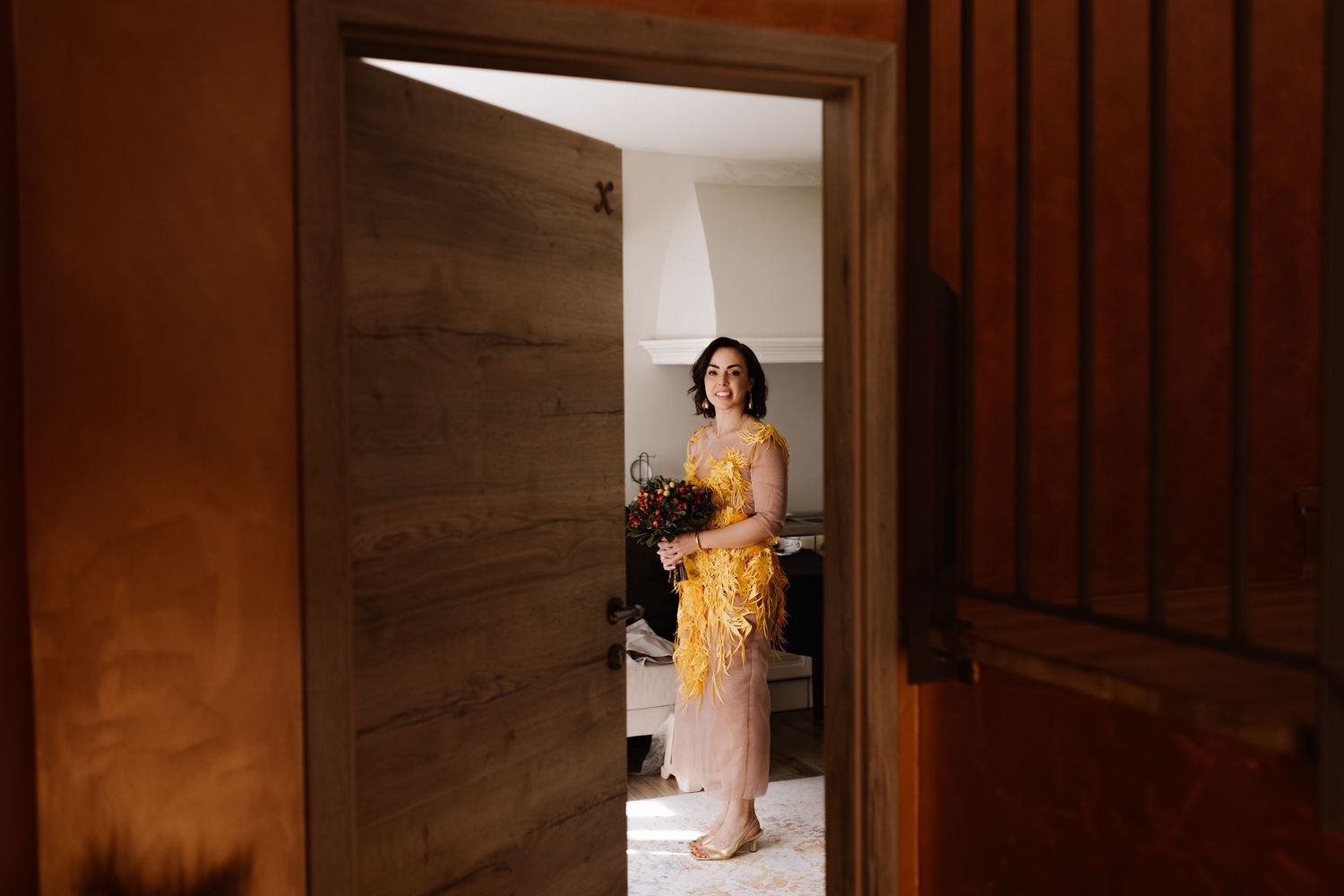 A bride in a white wedding dress walks down a dark wooden hallway with dramatic lighting and shadows.