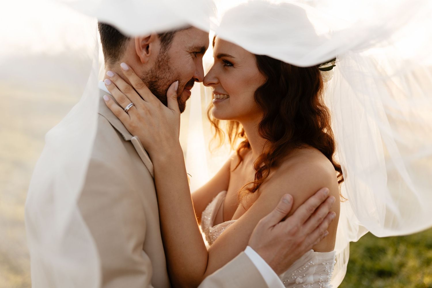 Romantic wedding portraits captured through flowing white veil in golden sunlight.