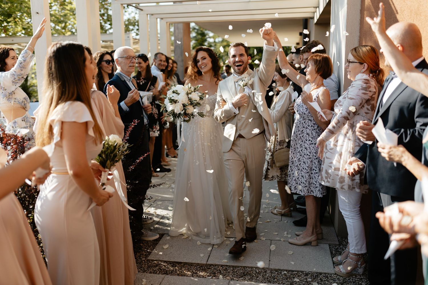 Wedding guests line up in a row outdoors while throwing white flower petals during a celebration exit.