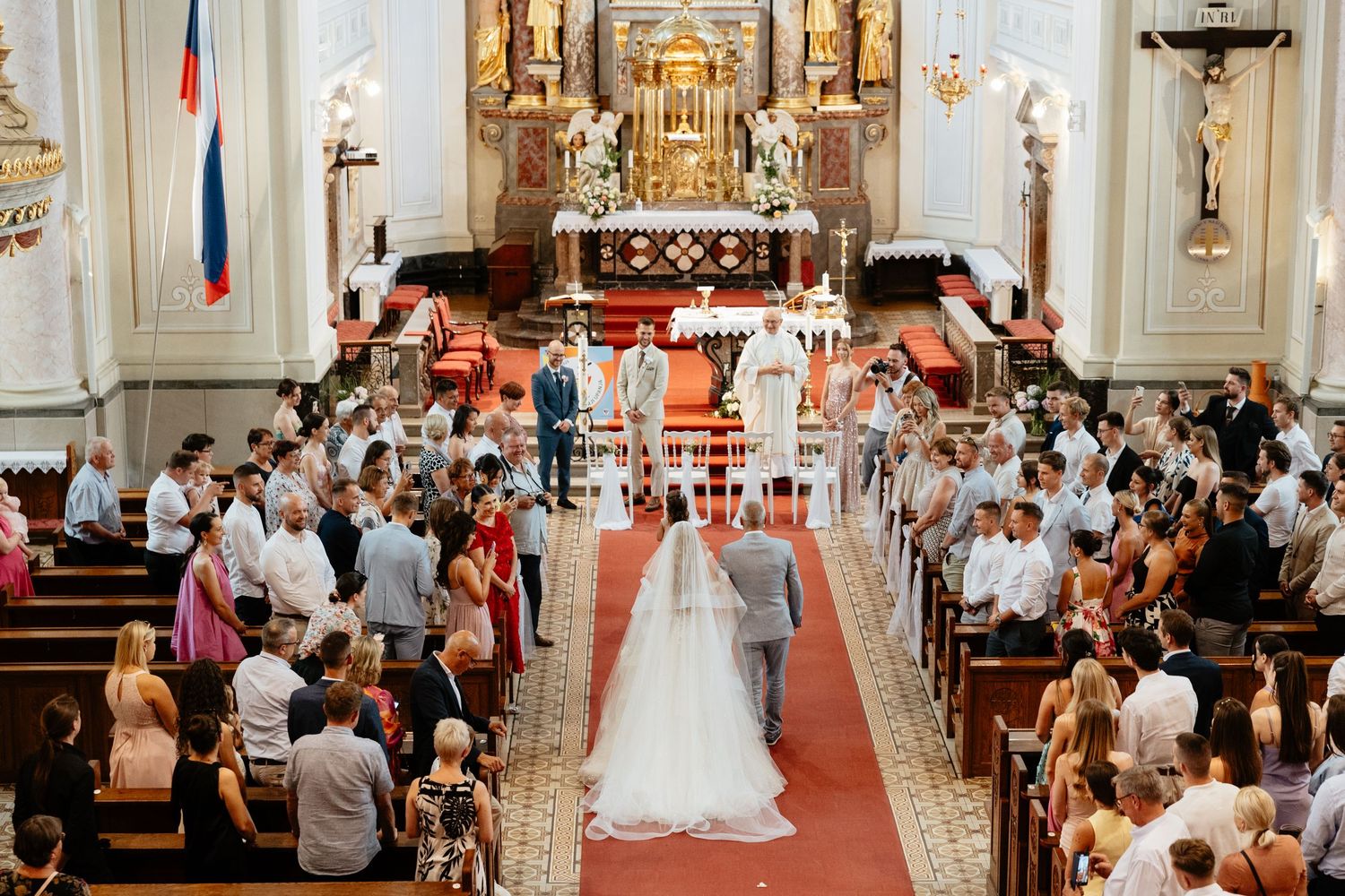 A traditional Catholic church wedding ceremony with guests seated in wooden pews and ornate altar decorations.