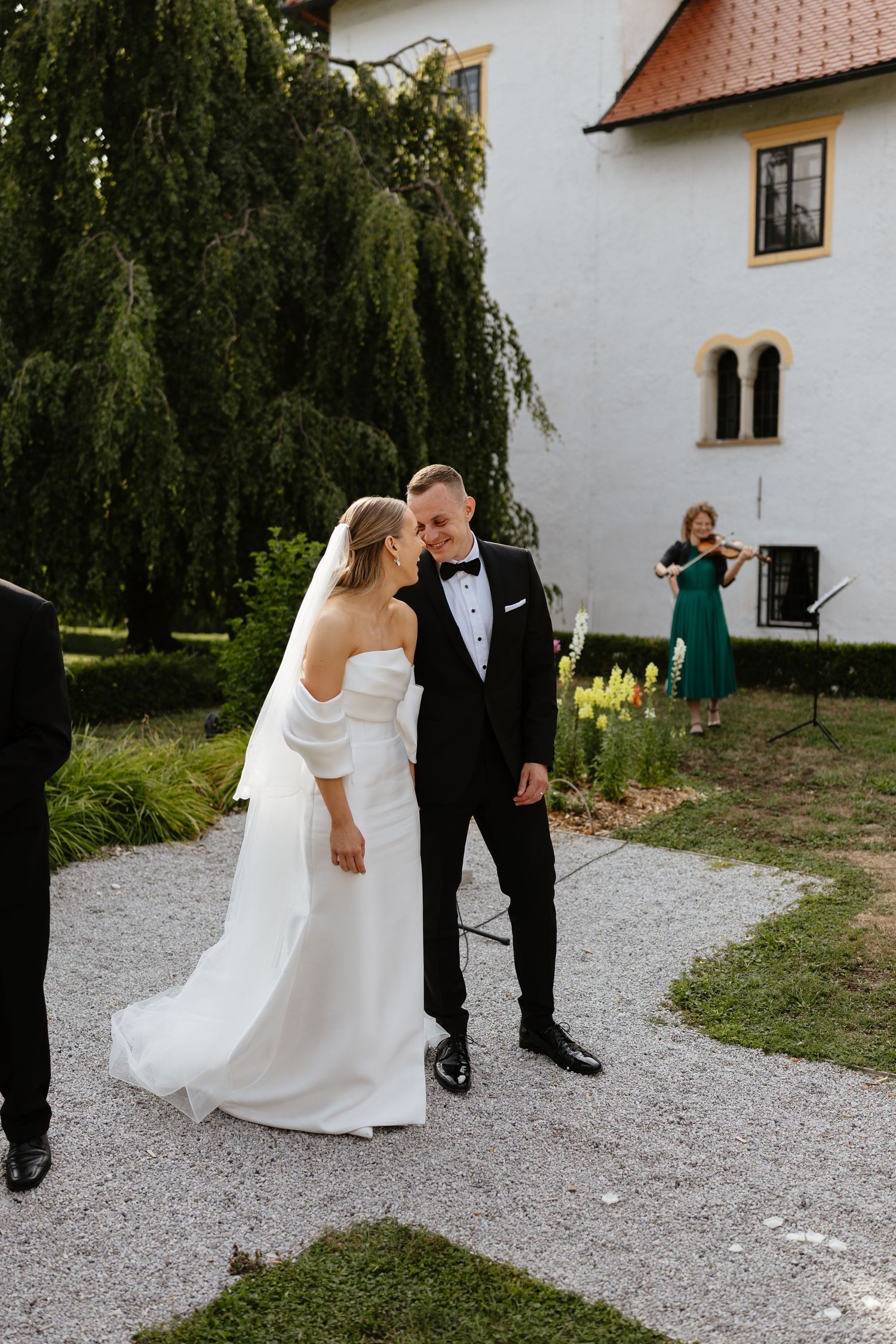 Elegant wedding couple posing outside historic building with weeping willow tree.