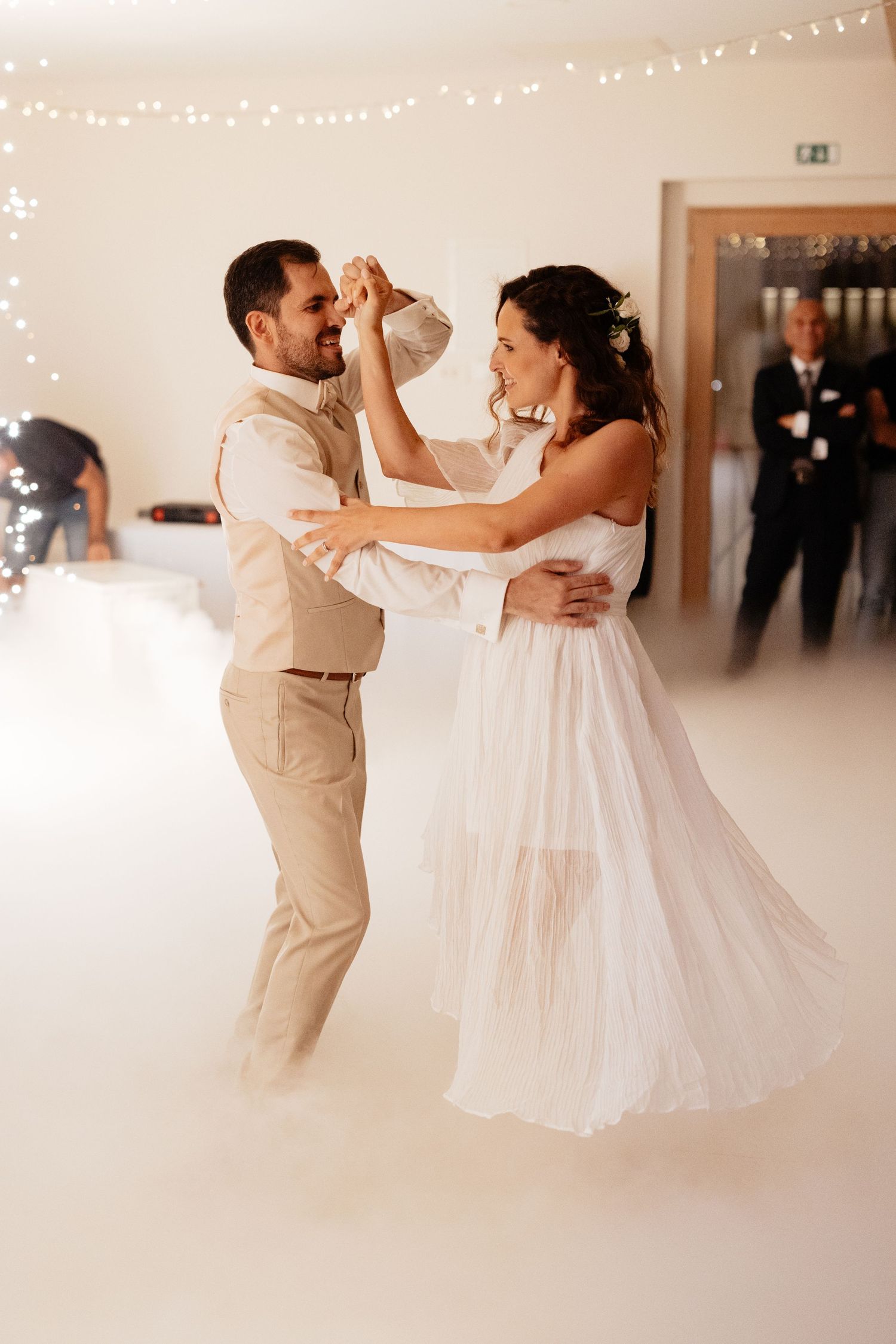 Wedding couple dances together under twinkling lights in bright indoor venue with romantic spins and twirls.