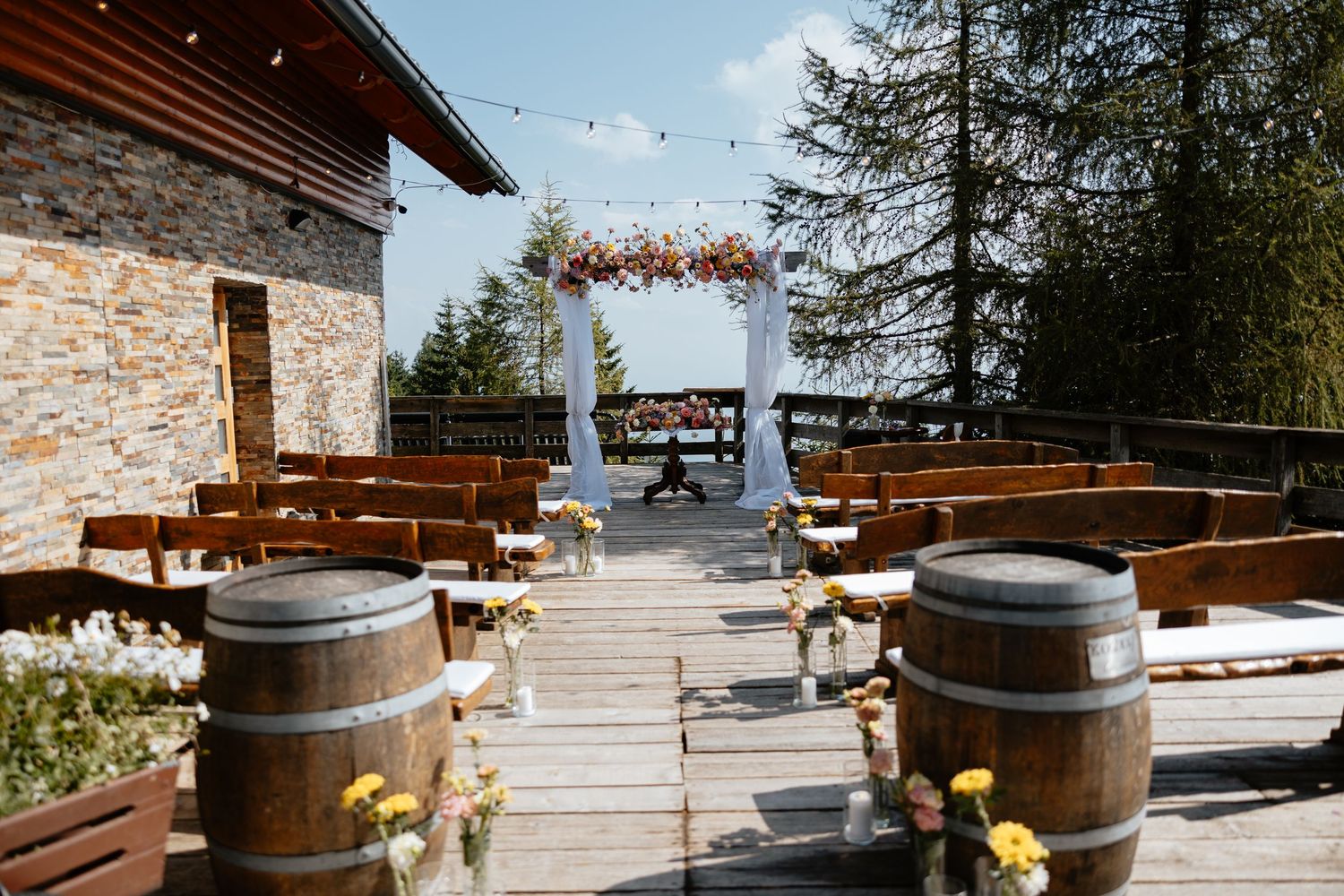 Rustic outdoor wedding venue with wooden barrels and mountain views on a sunny day.
