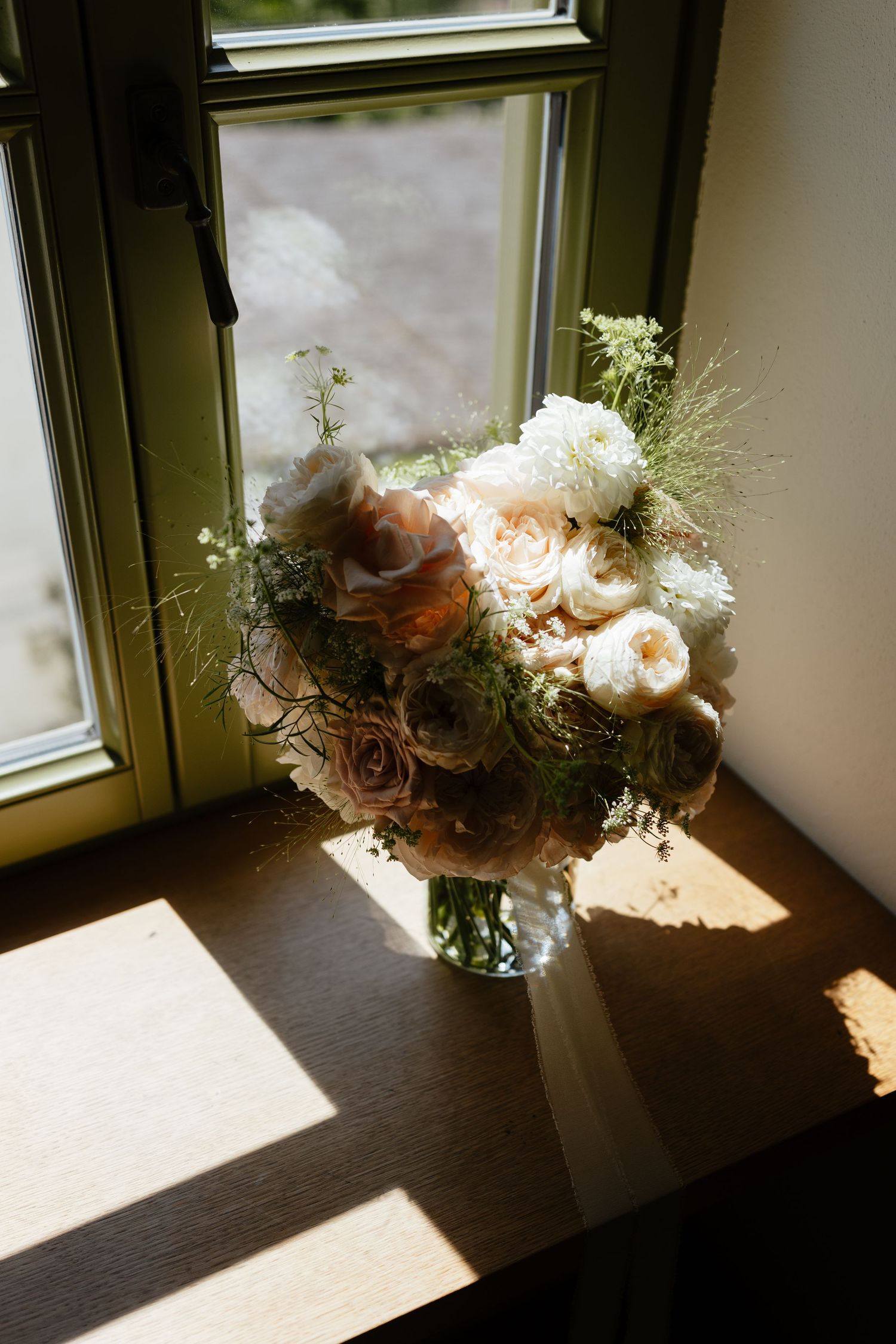 A romantic floral arrangement sits in sunlight by a window creating dramatic shadows.