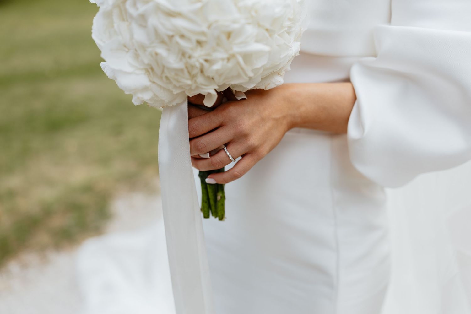 Close-up details of a flowing white wedding dress and bouquet against a natural outdoor setting.