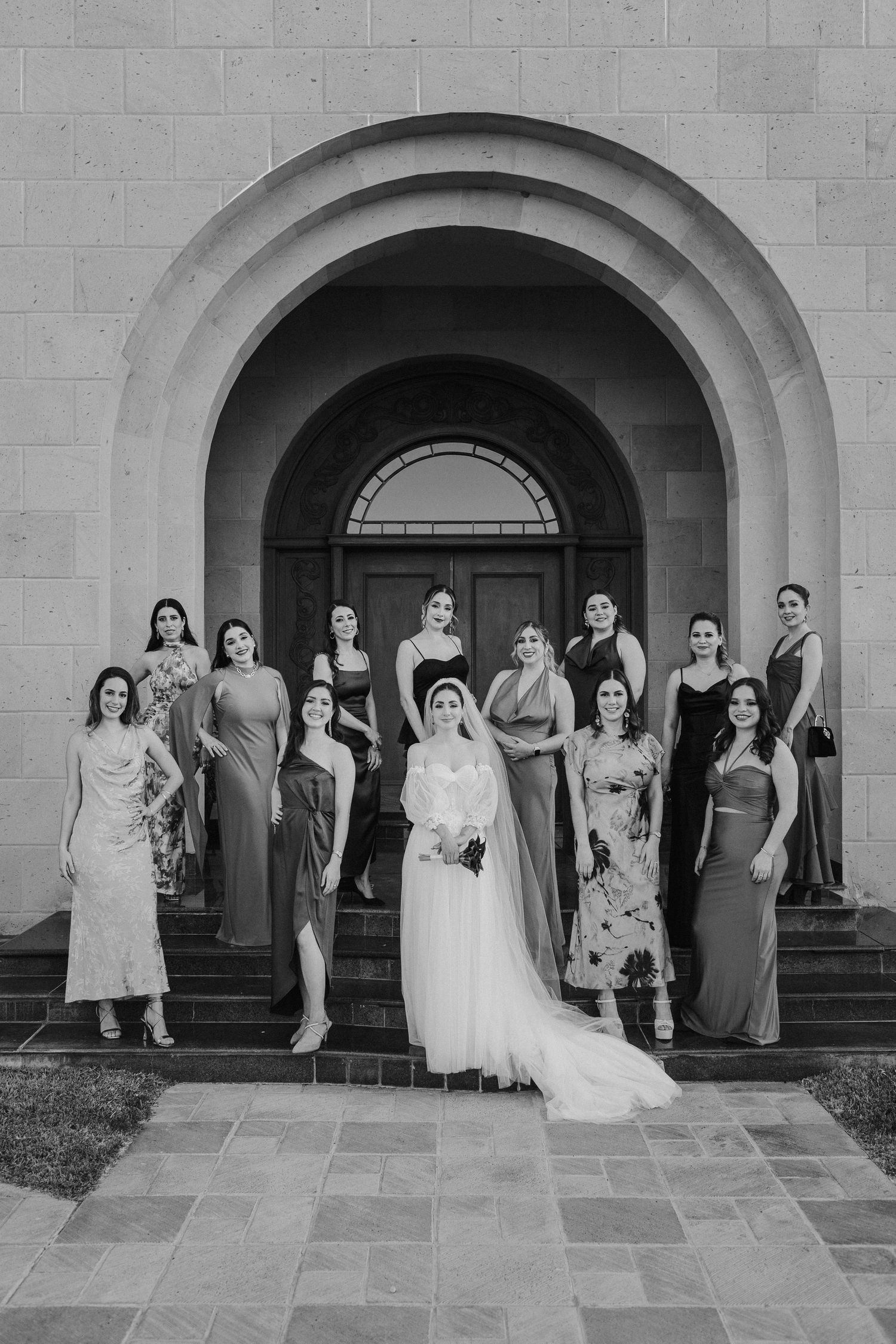 A black and white photo series showing a wedding party posing under stone archways at an elegant venue.