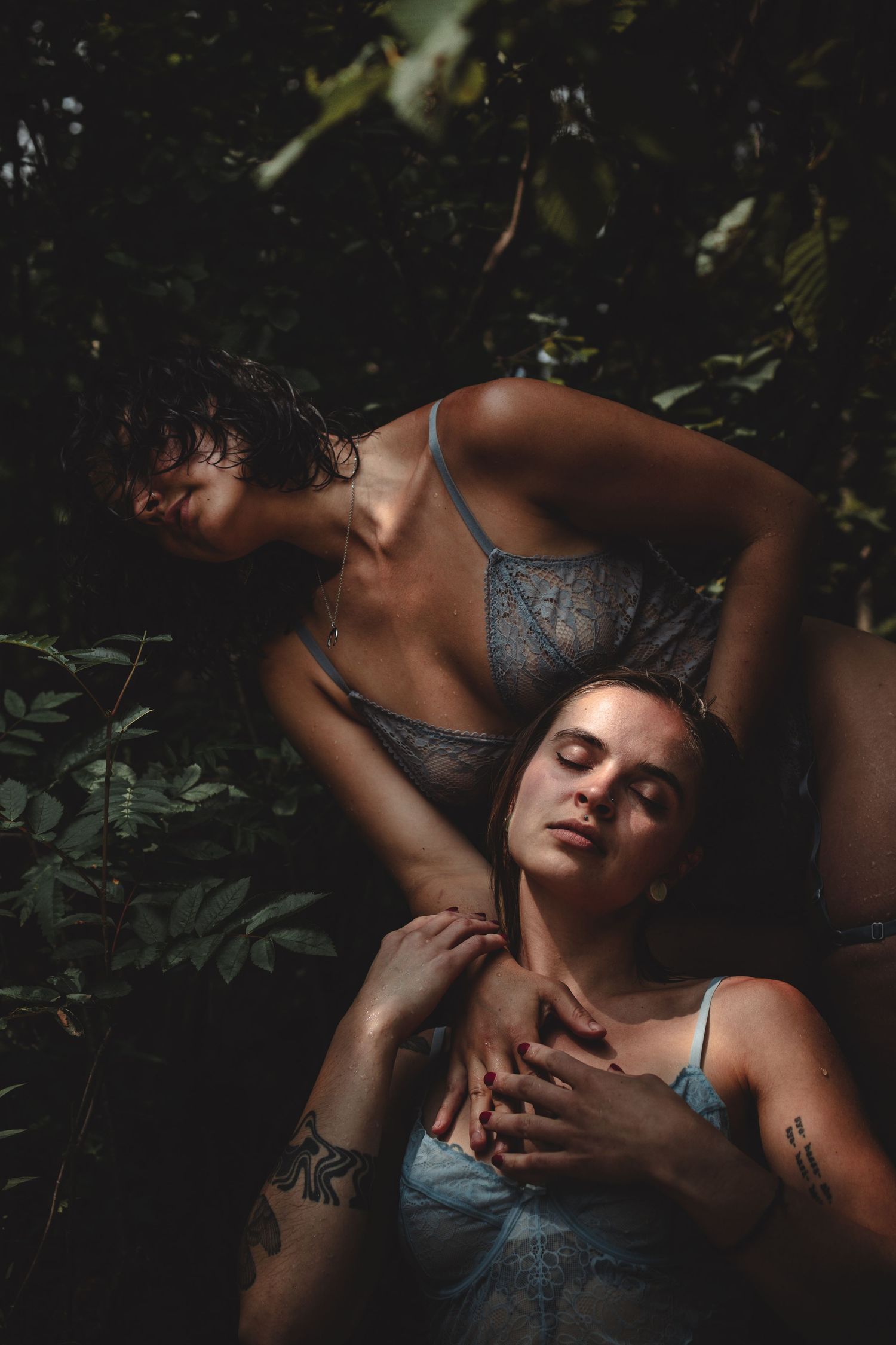 Intimate portrait of two people in lace lingerie surrounded by foliage.