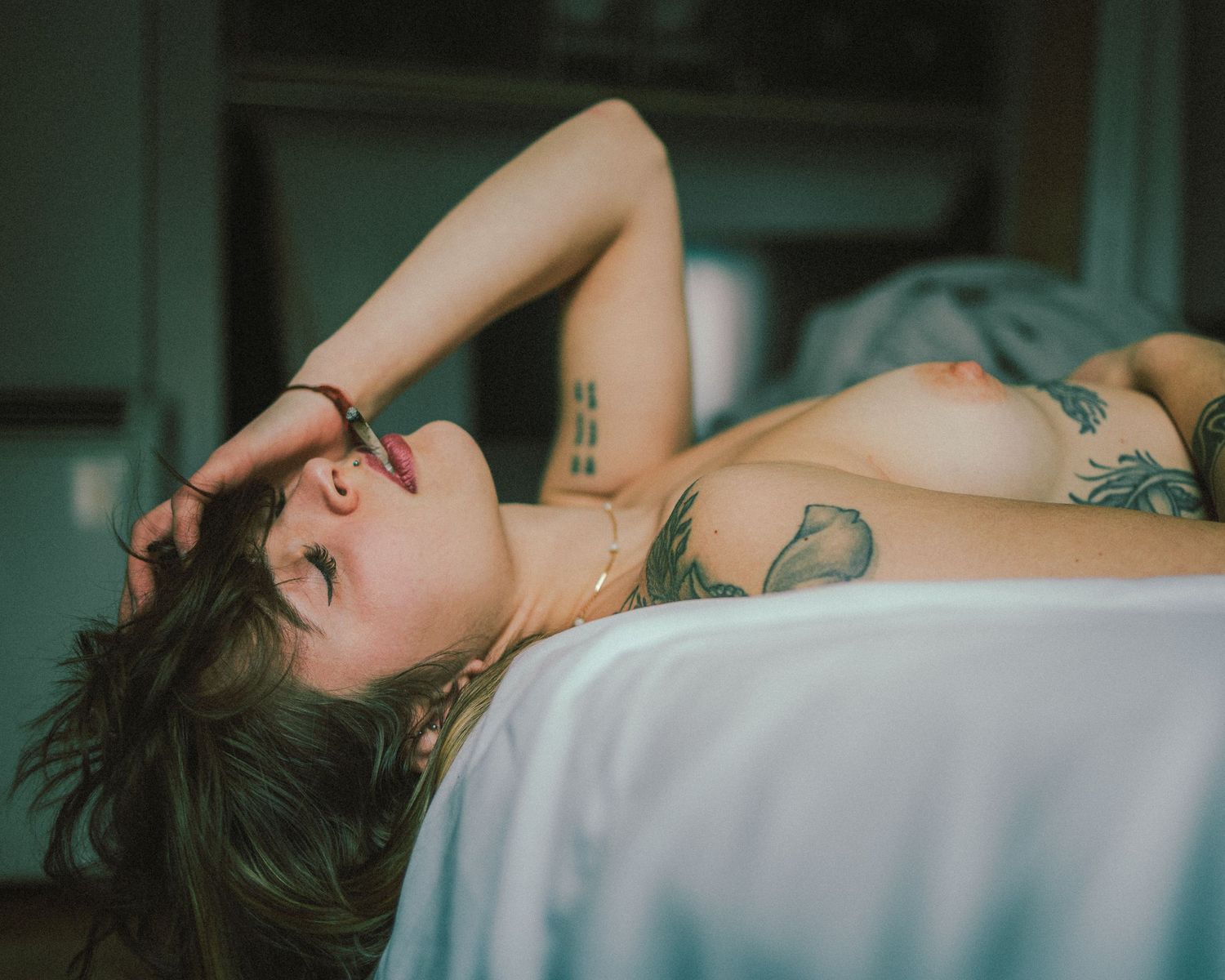 Person lying on bed in relaxed pose with soft teal lighting creating dreamy atmosphere.
