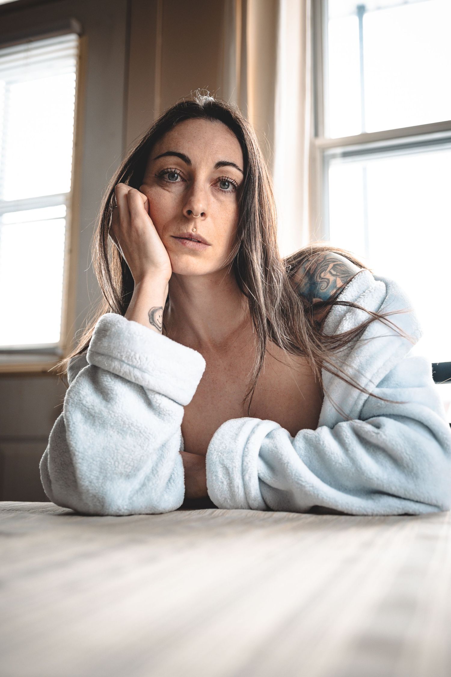 Person in white sweater lying on white surface in soft window light.