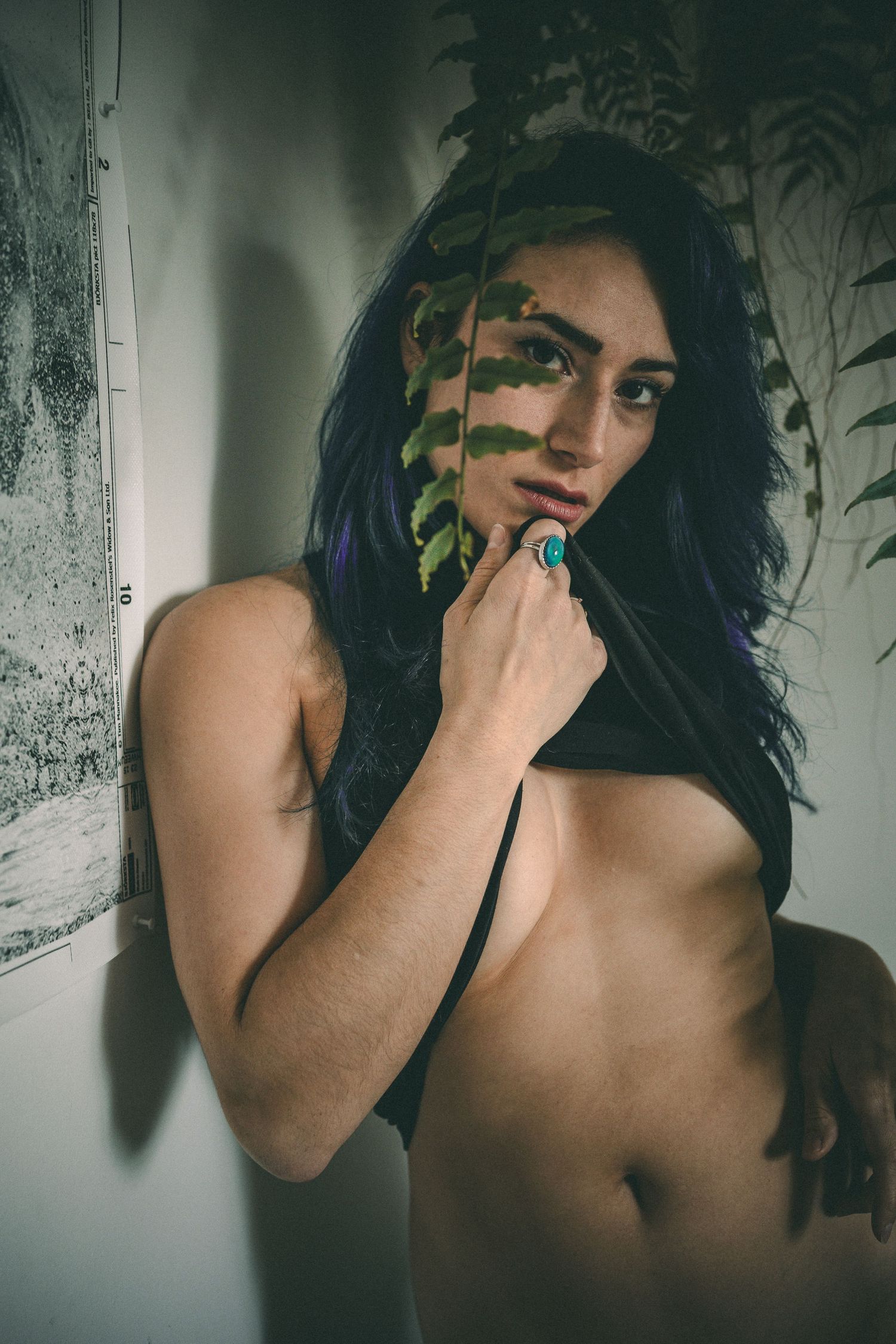 Artistic portrait with blue hair against wall with plant shadows creating dramatic effect.