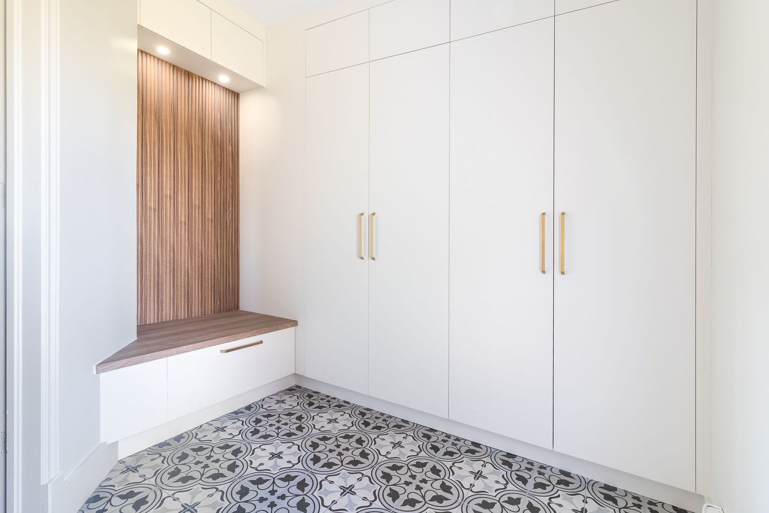 White built-in storage cabinets with wooden accents and contemporary hardware in a bright room.