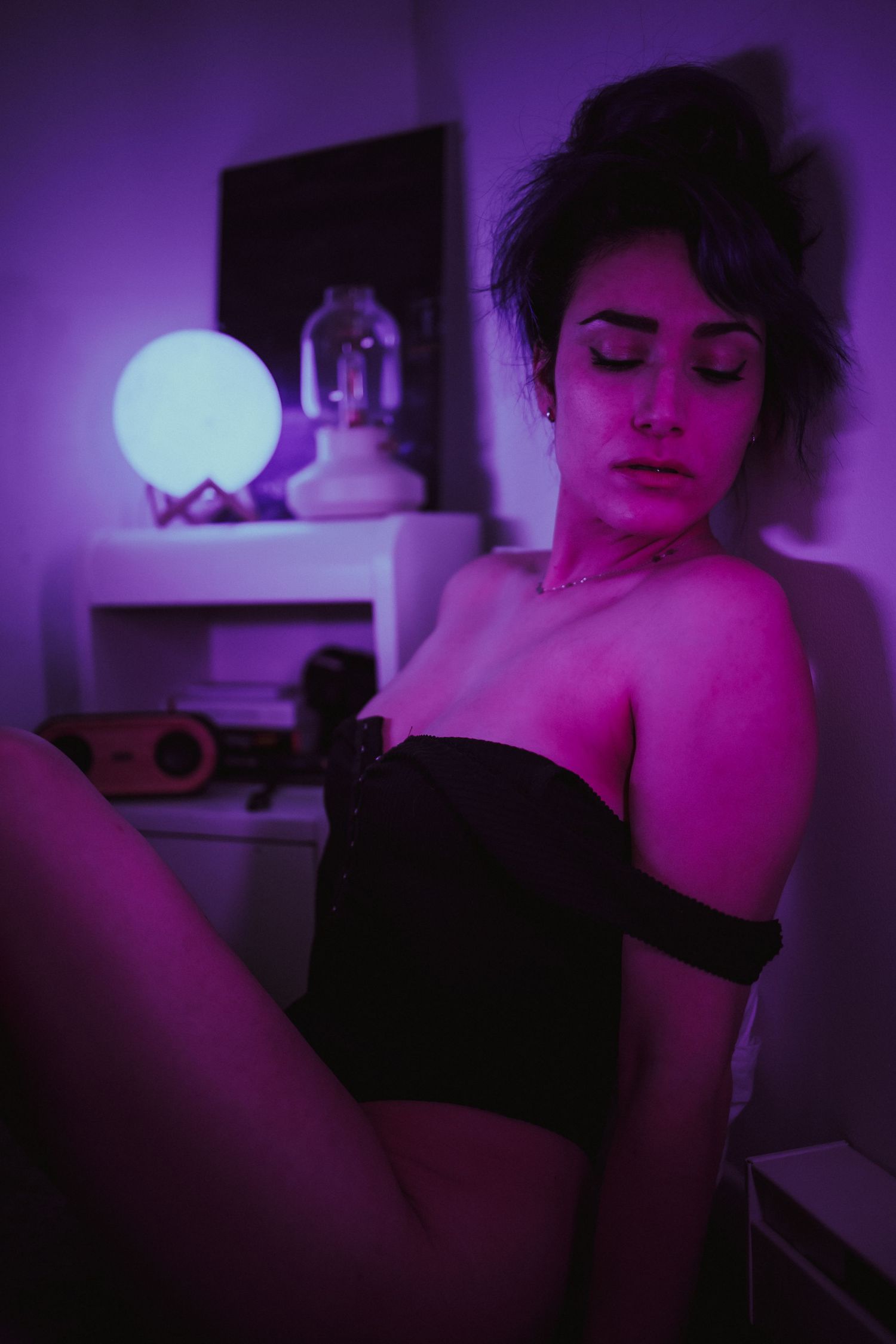Artistic boudoir photo with purple lighting and glowing moon lamp on nightstand.