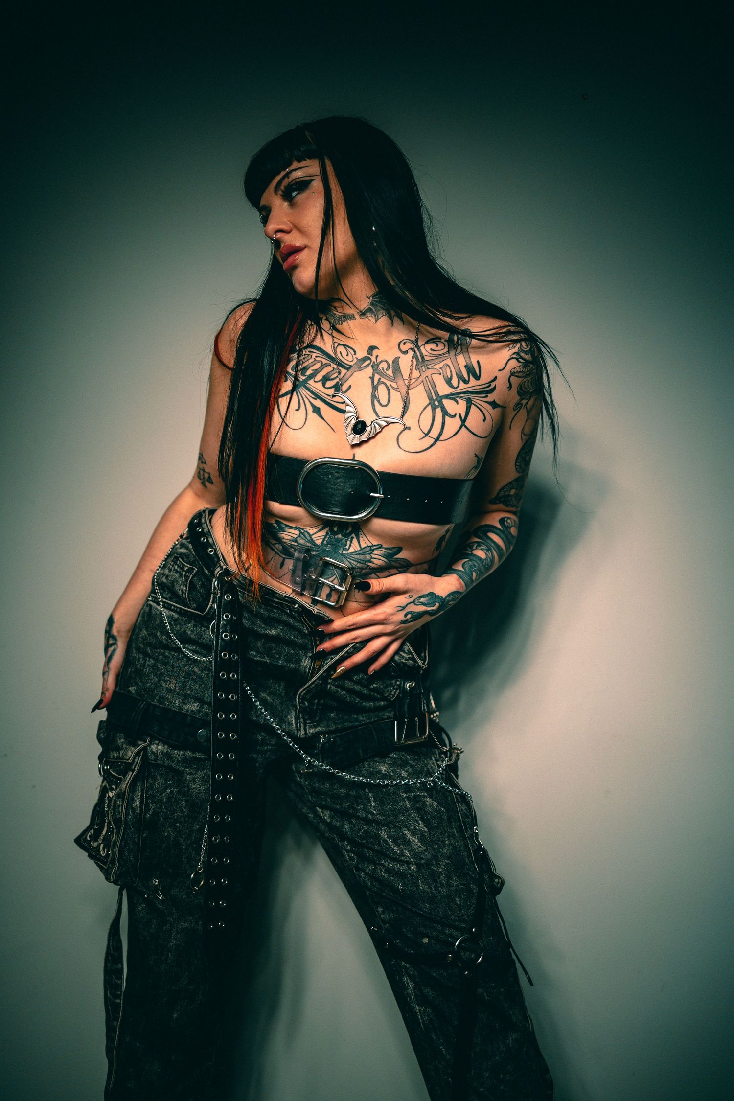 Gothic fashion portrait with black clothing and tattoos against white background.