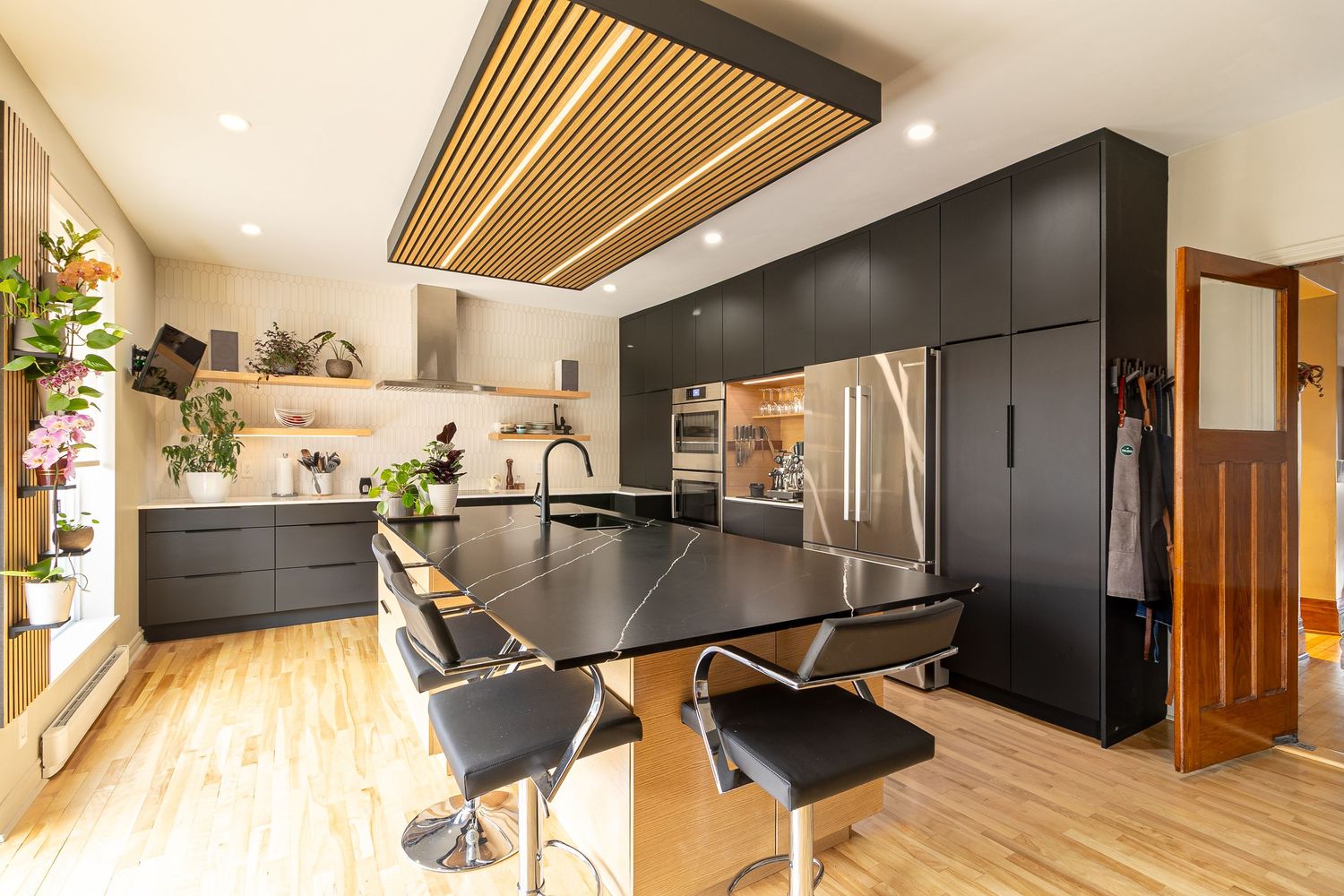 Spacious modern kitchen with black cabinets and wood accents shown from multiple angles.