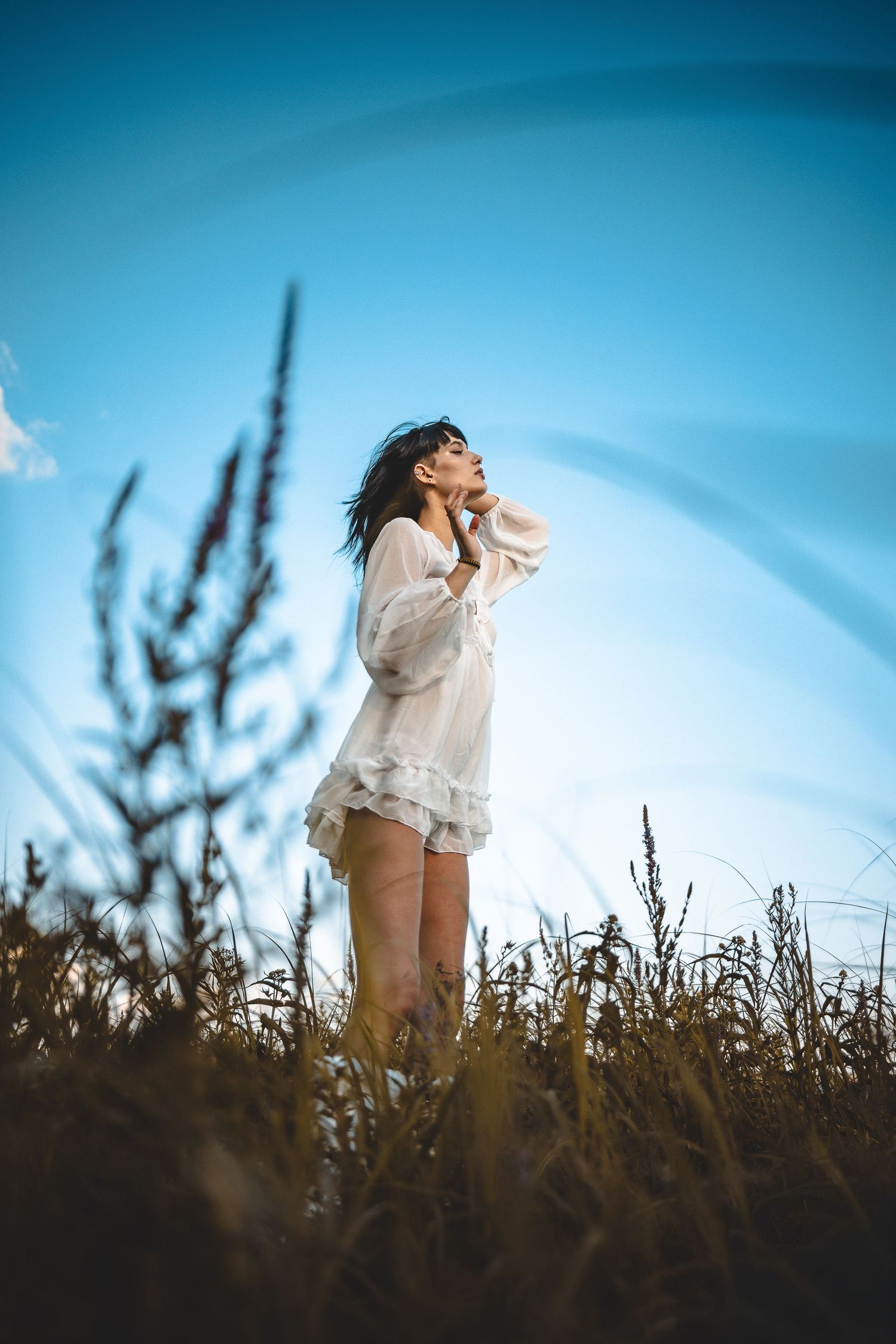 Ethereal outdoor photoshoot in a field at golden hour with dreamy blue sky backdrop.