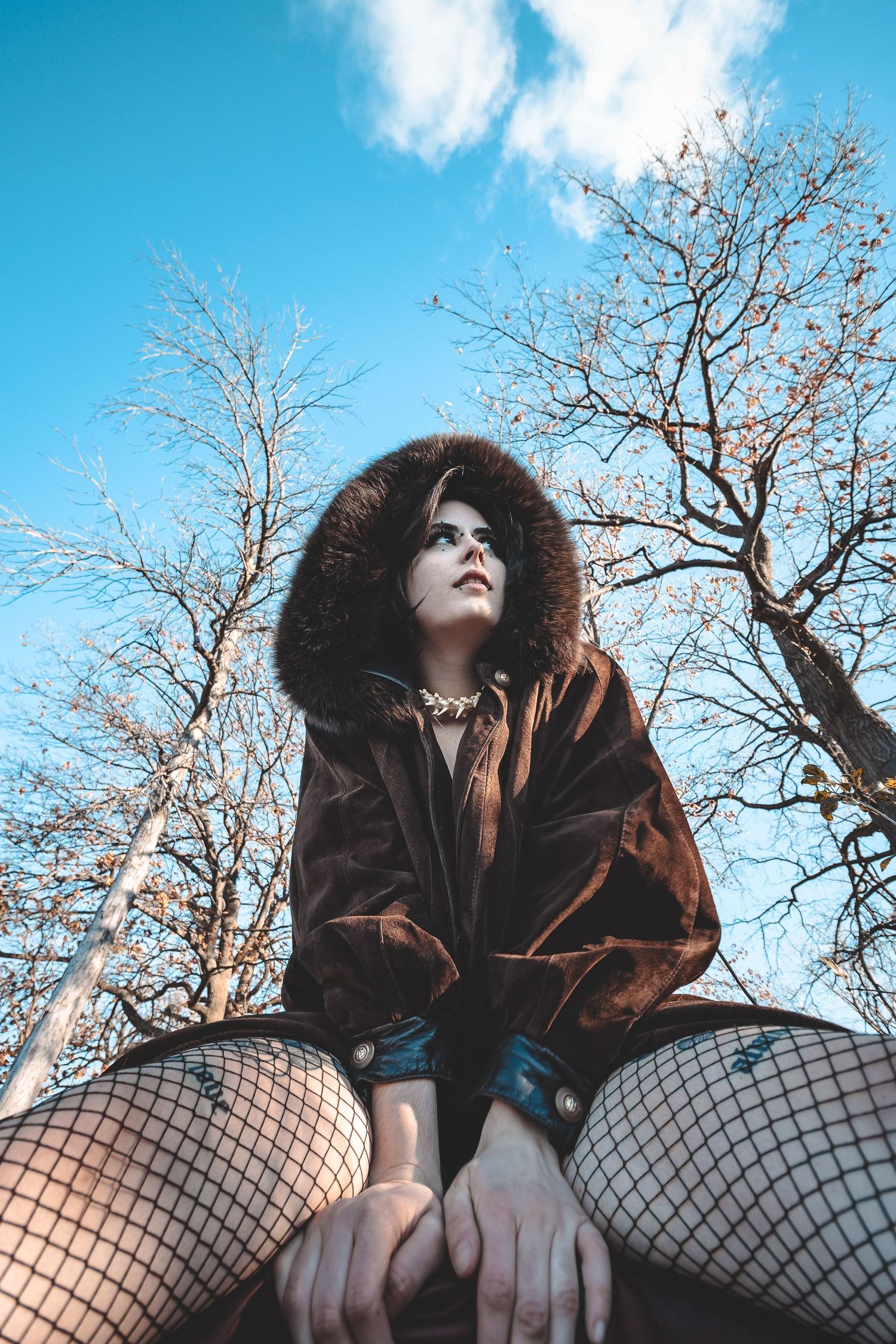 Alternative style fashion shoot with fishnets and leather against bare winter trees.