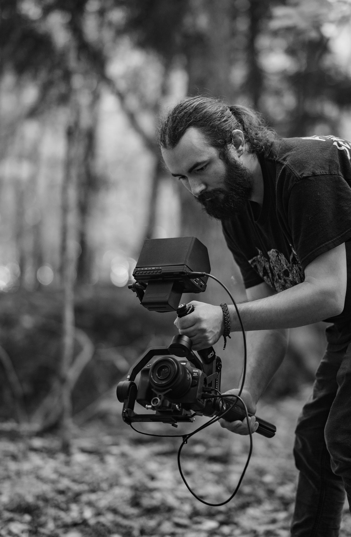 Black and white image of camera operator filming in forest setting.