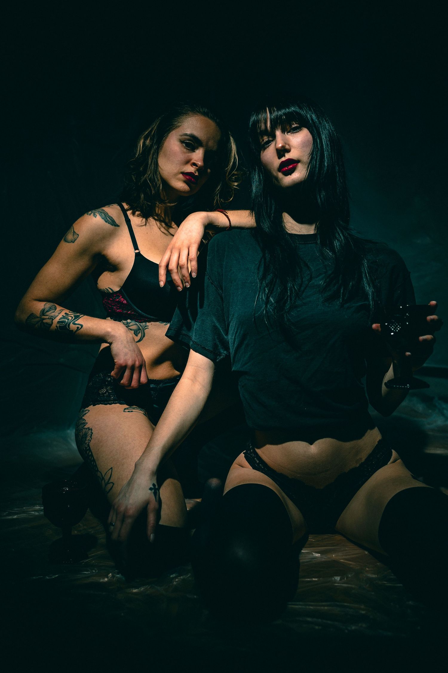 Dark and moody portrait of two people in black lingerie against dark background.