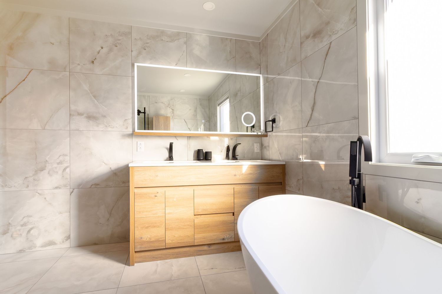 Spa-like bathroom with marble walls, wooden storage cabinets, and a modern freestanding soaking tub.